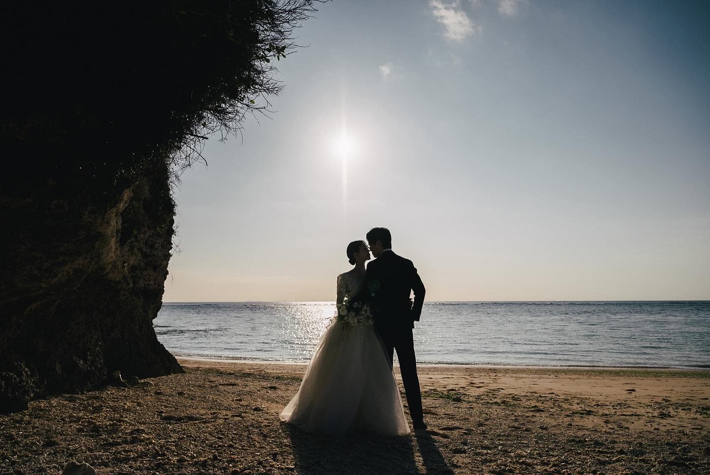 Silhouetted couple stand close on a sunlit Okinawa beach