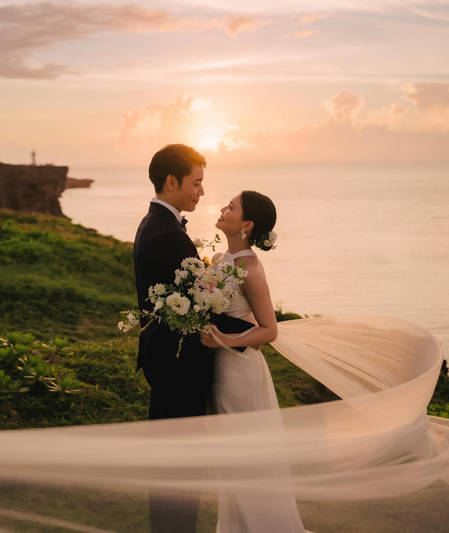 Bride and groom face to face at sunset sea, veil in the wind, Okinawa