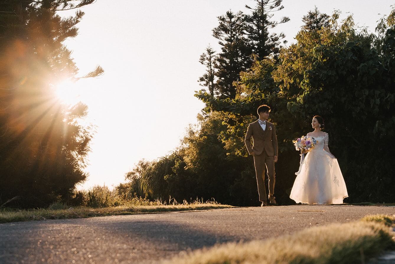 Bride and groom walking down a tree-lined road in Okinawa as the setting sun flares through the trees
