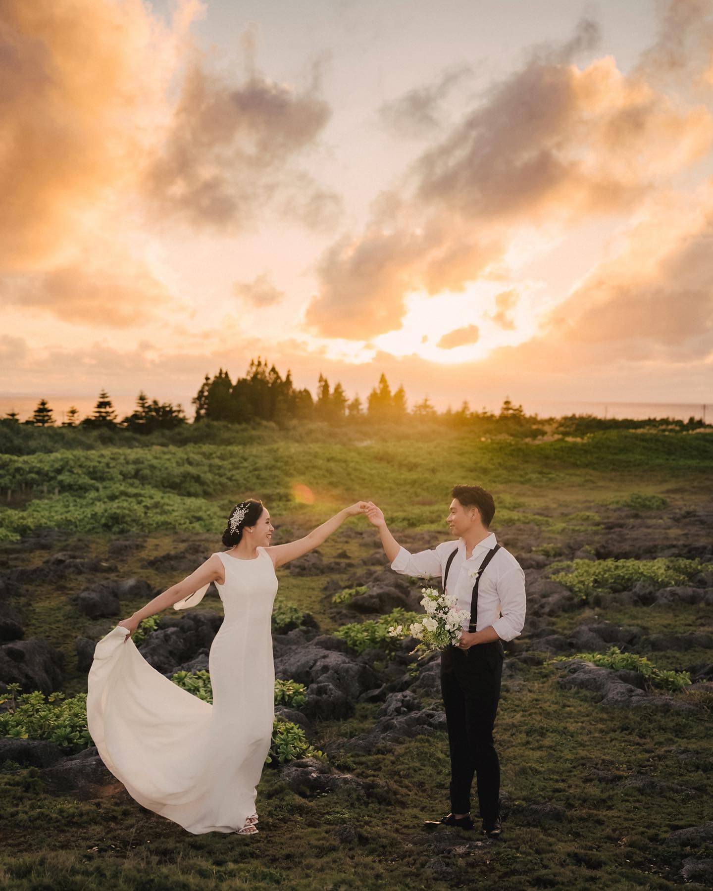 Bride and groom dancing on a rocky meadow at sunset in Okinawa