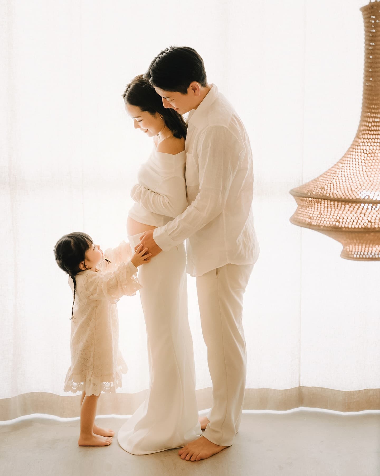 A girl reaches for her pregnant mother's bump in a bright studio