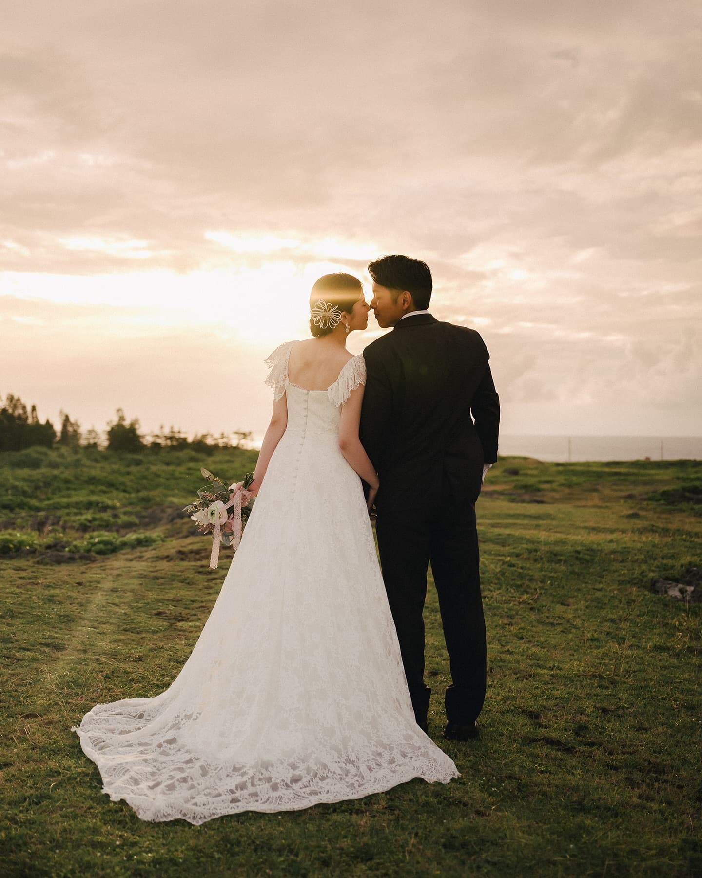 Back view of a couple leaning close on a grassy field at sunset in Okinawa