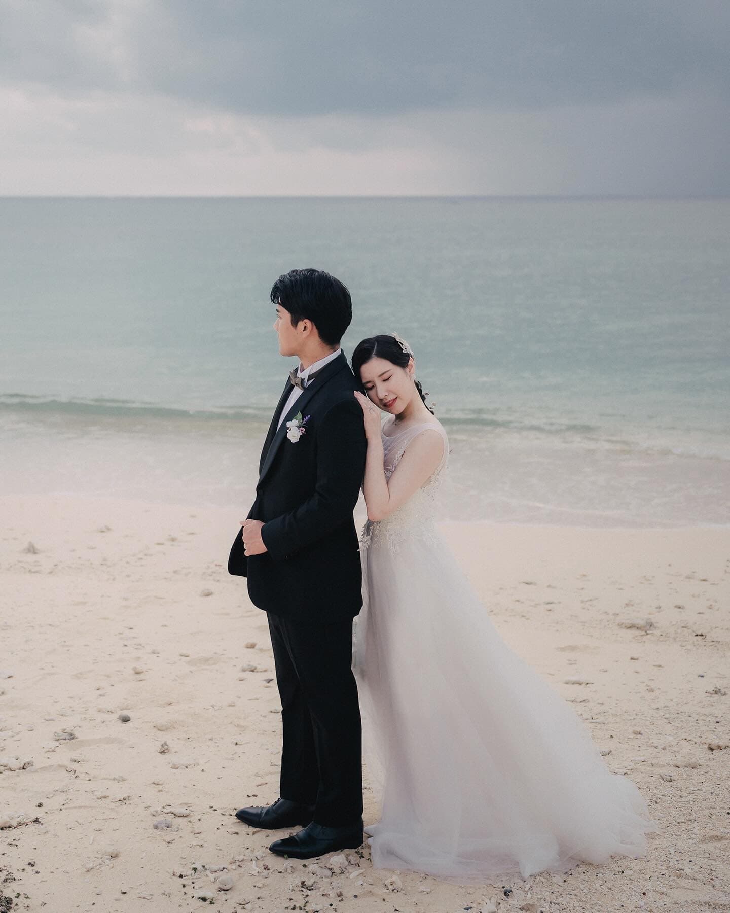 Bride leaning gently on the groom's shoulder on an overcast Okinawa beach