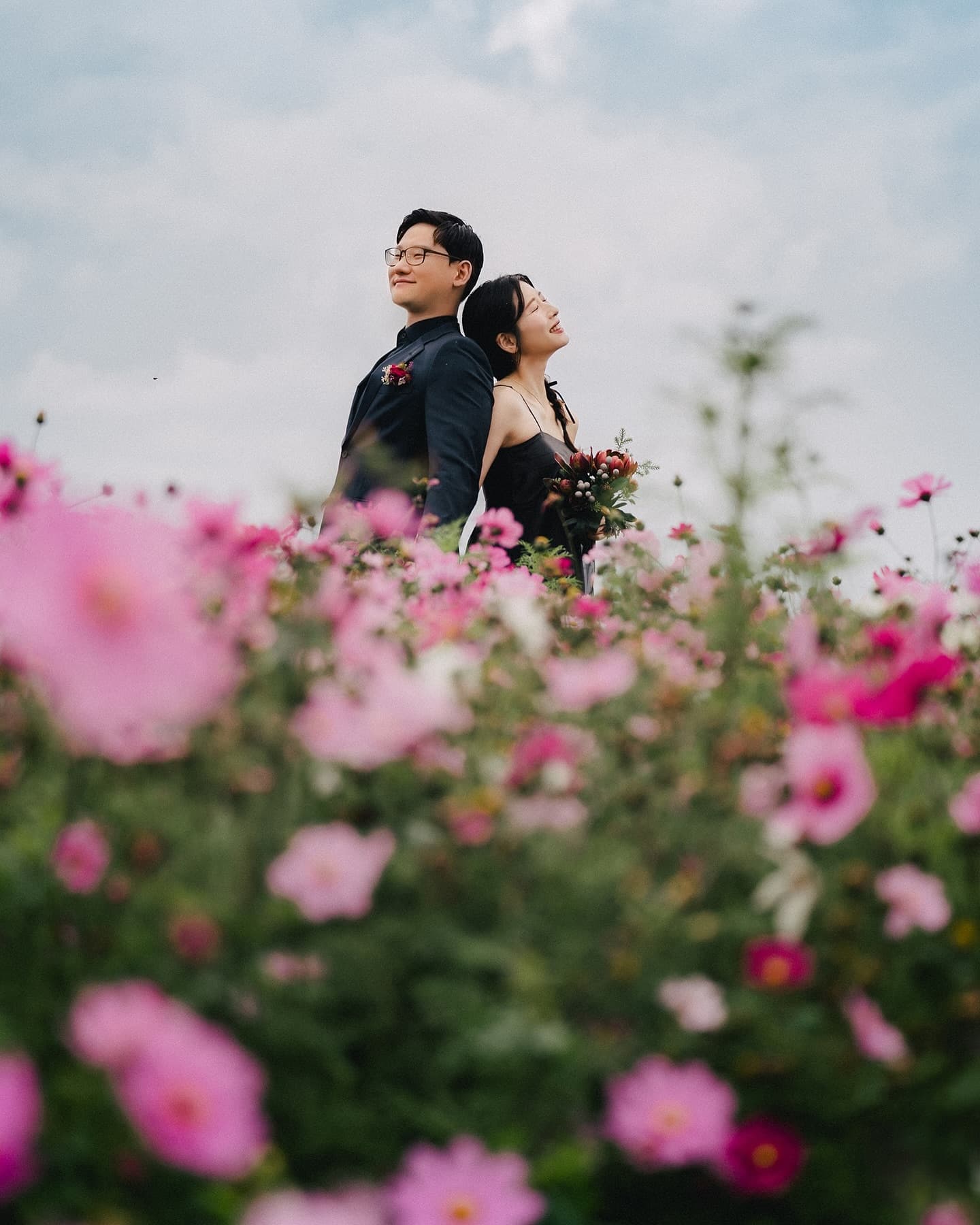 Couple in black stand back to back in a cosmos field in Okinawa