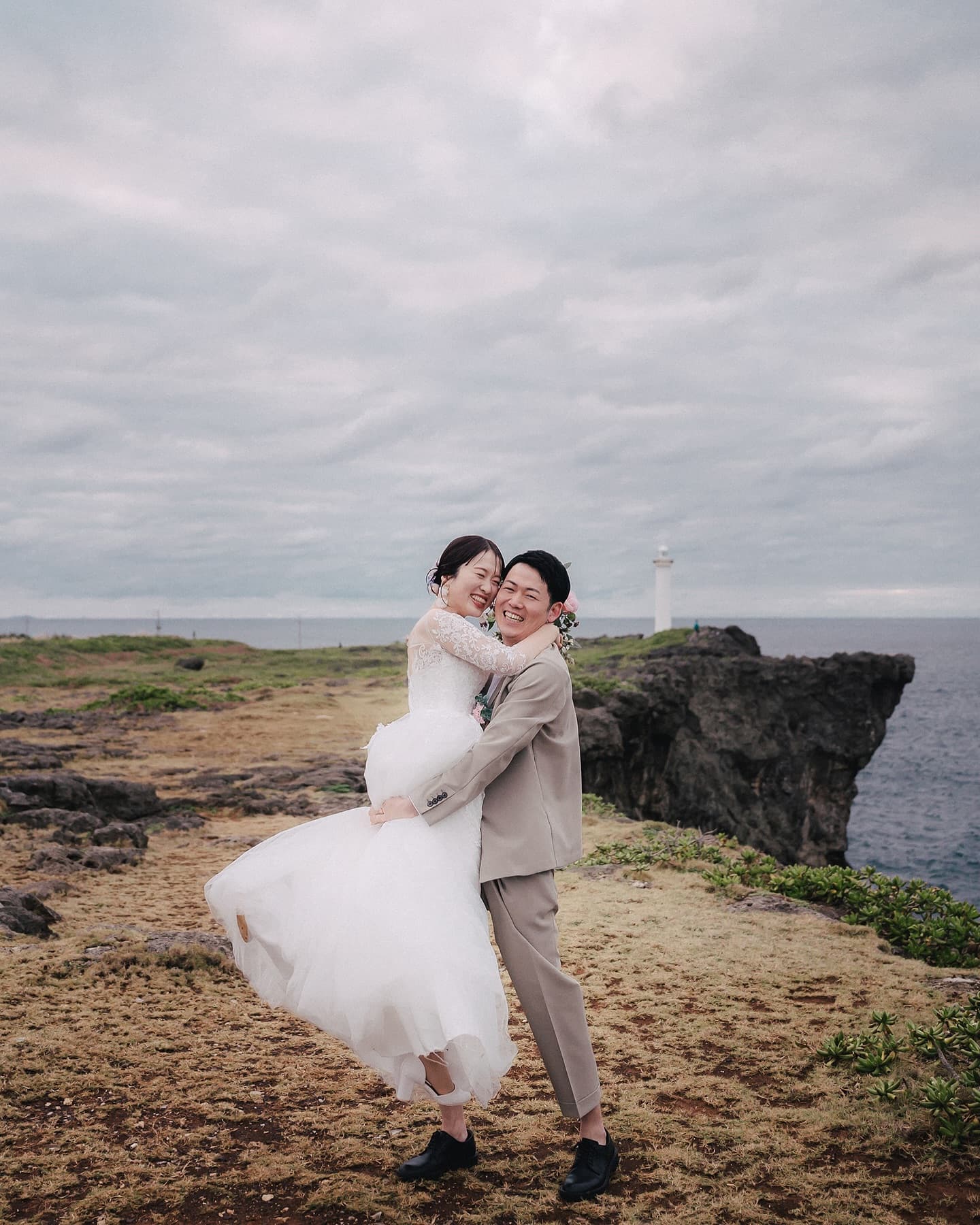 Groom lifting his laughing bride near a lighthouse in Okinawa