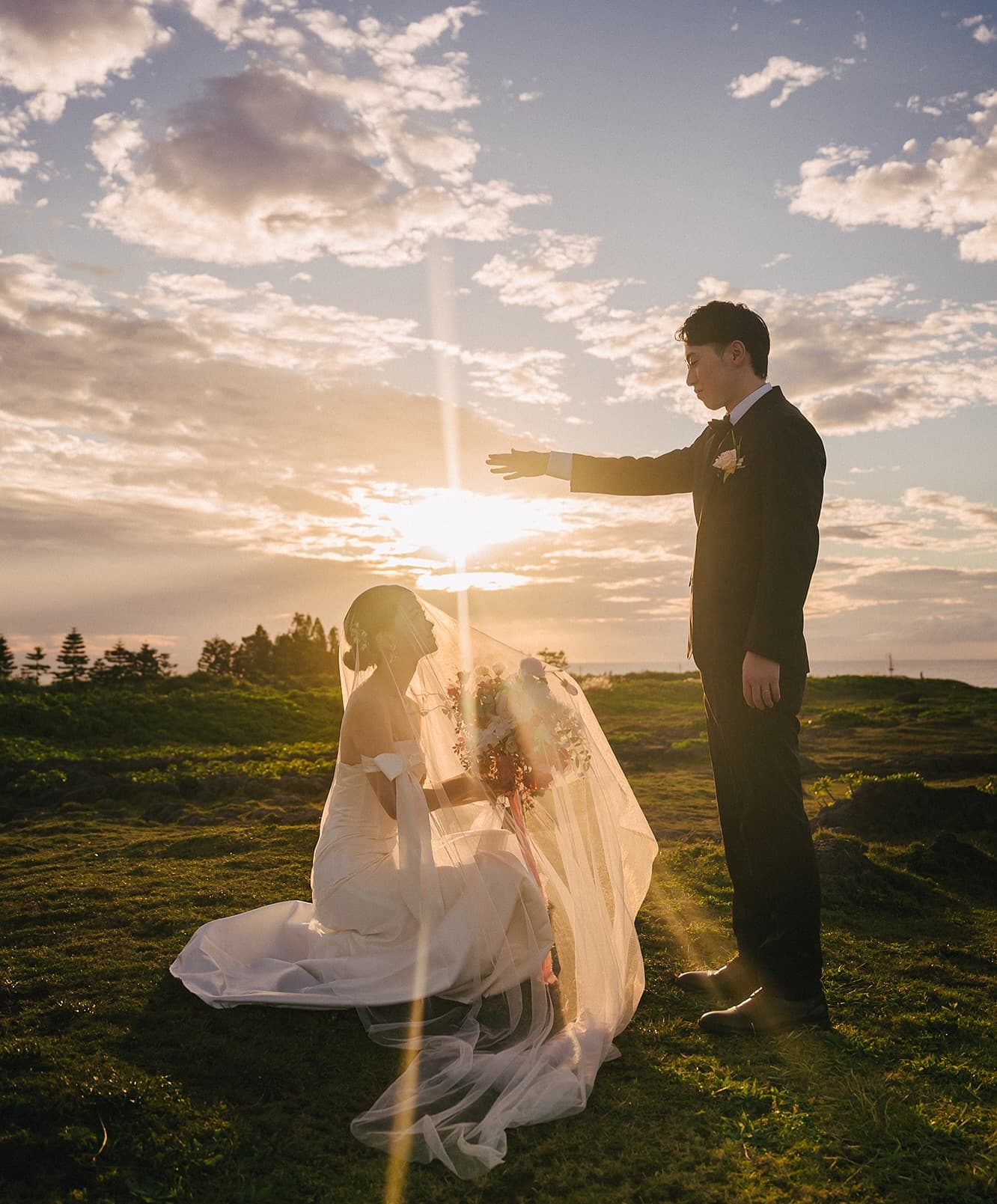 夕焼けの丘でひざまずく花嫁に手を差し伸べる新郎、沖縄の前撮り