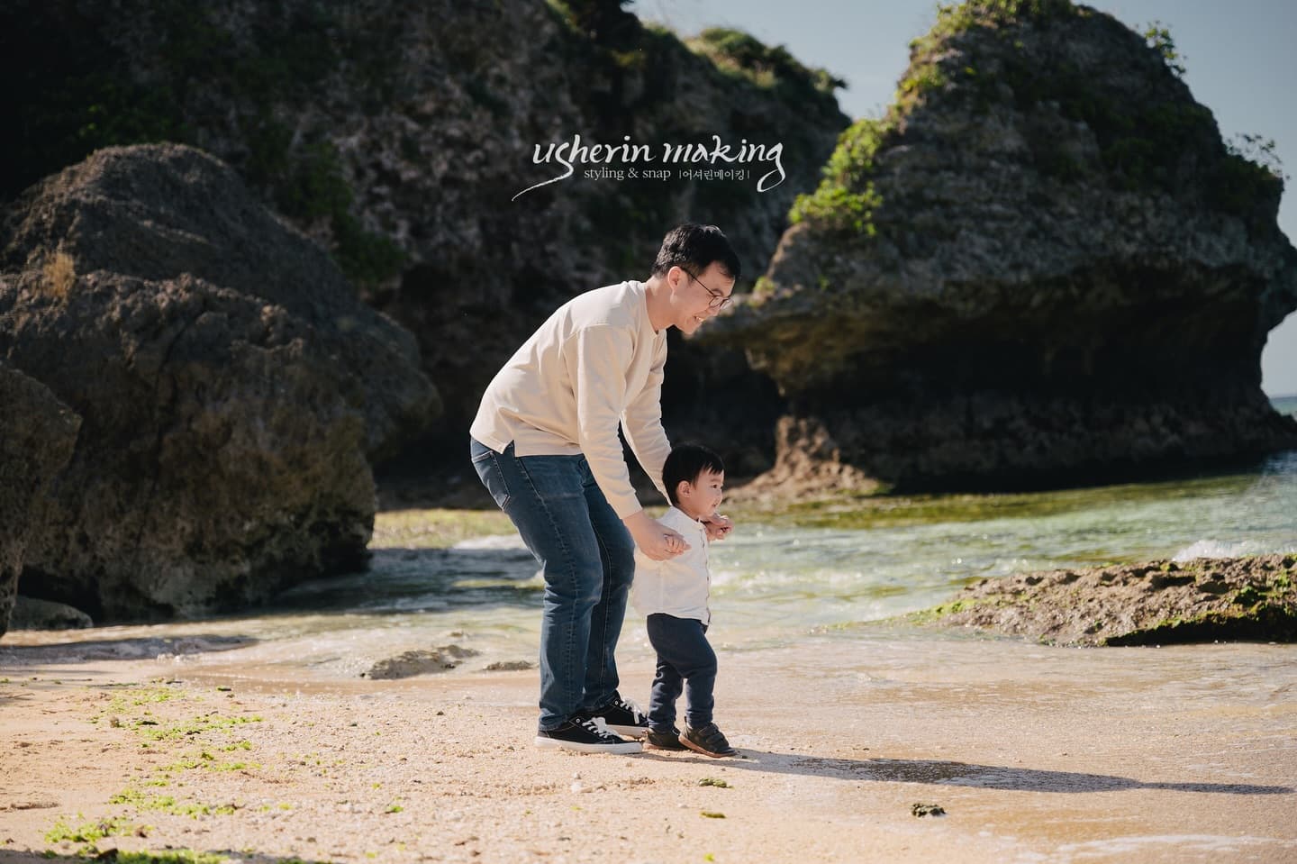 Father steadying his toddler at the water's edge by the rocks on an Okinawa beach