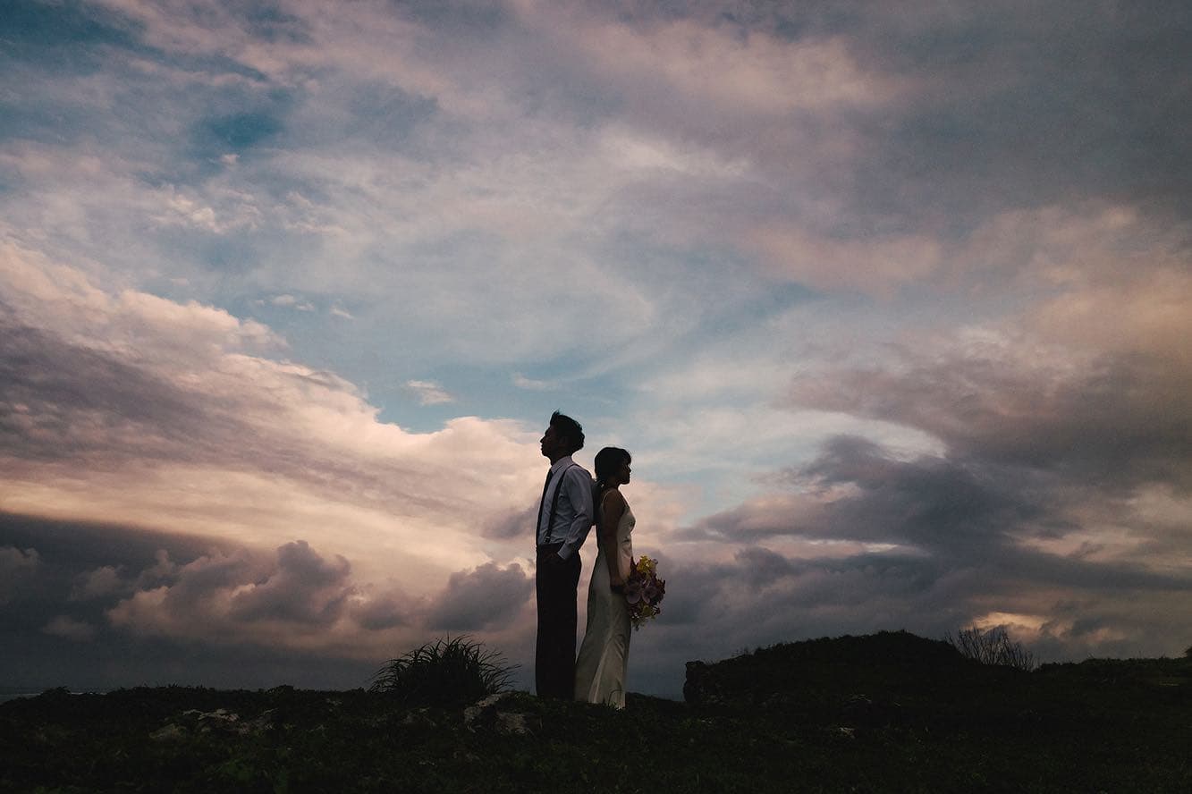 Silhouetted couple standing back to back against a dramatic sunset sky in Miyakojima