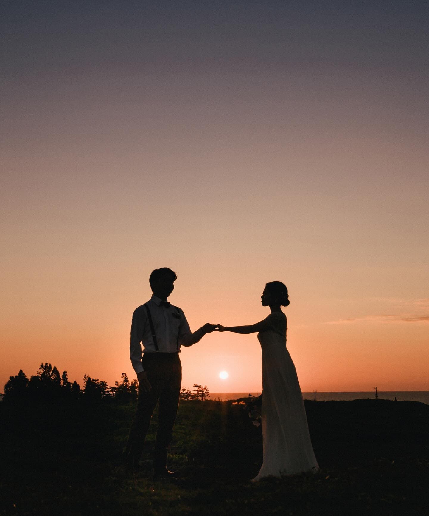 Silhouetted couple joining hands as the sun sinks to the horizon in Okinawa