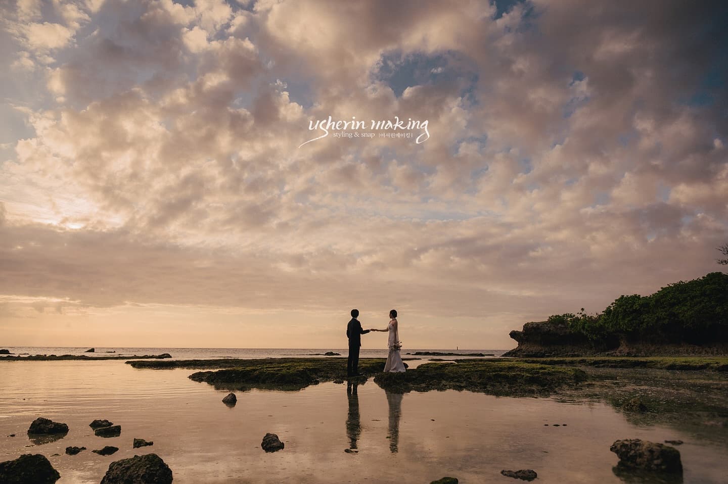Wide sunset view of a couple facing each other on tidal rocks under glowing clouds in Okinawa