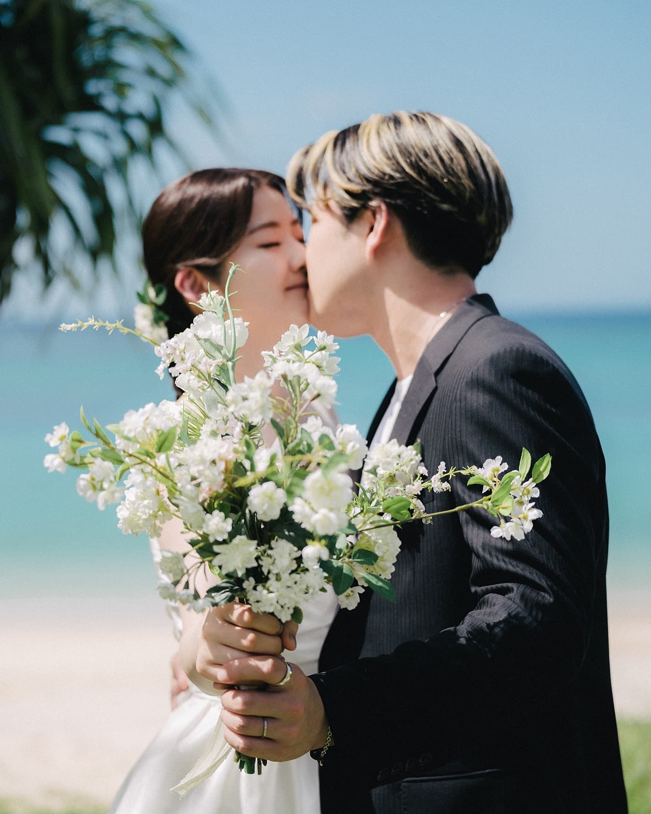 Bride and groom kissing with a white bouquet against the blue sea in Okinawa