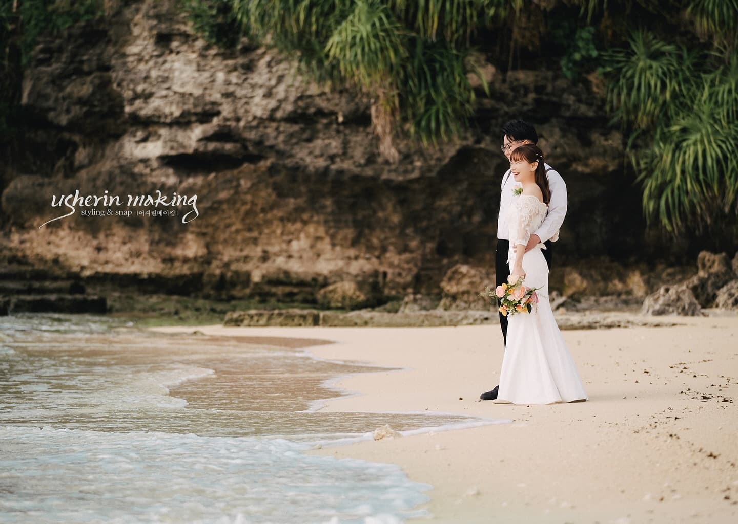 Couple strolling along the shoreline beneath a green cliff on an Okinawa beach