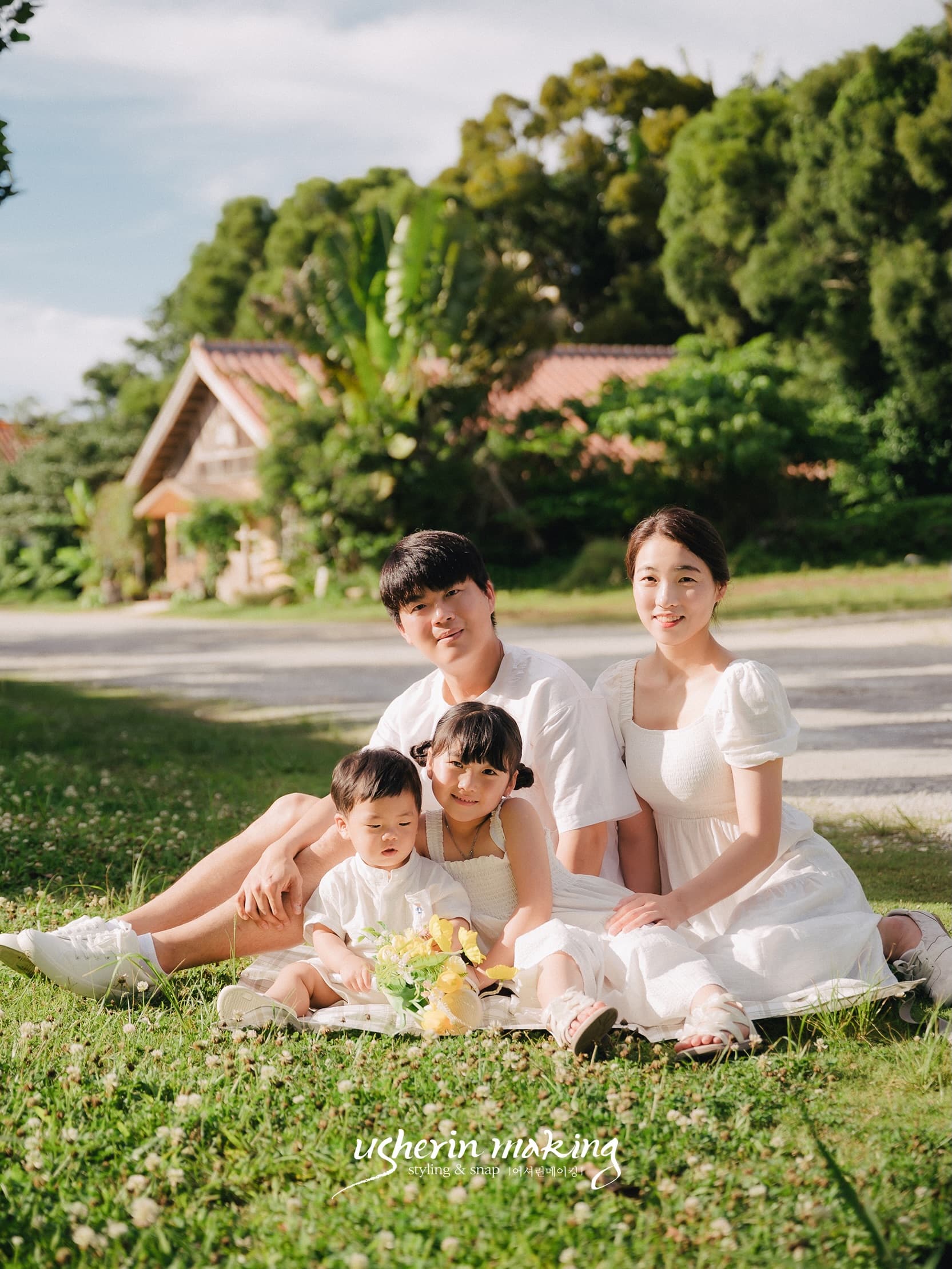 Family of four sitting together on a sunny lawn before a red-roofed Okinawa house