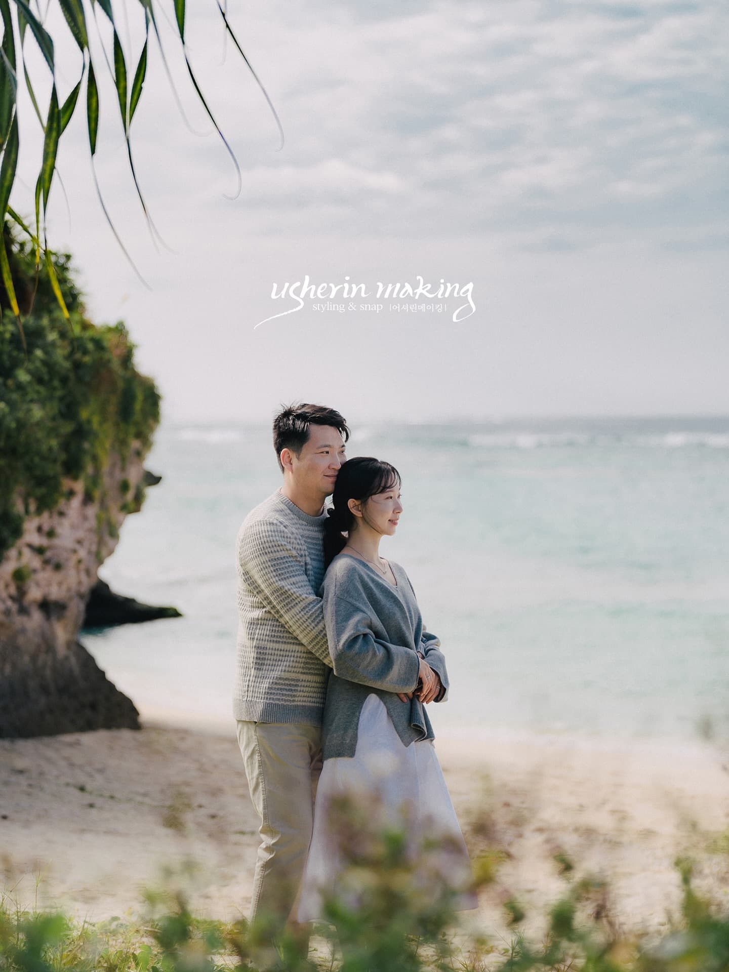 Couple embracing on a rocky Okinawa beach, gazing at the sea in soft overcast light
