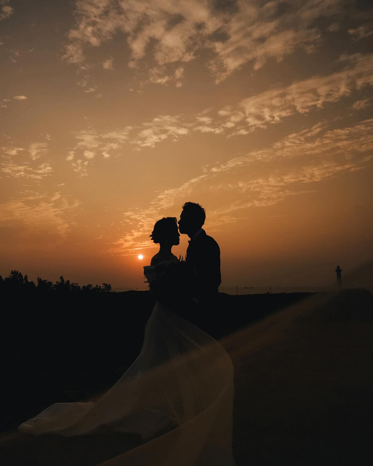 Silhouetted couple kiss against a glowing Okinawa sunset