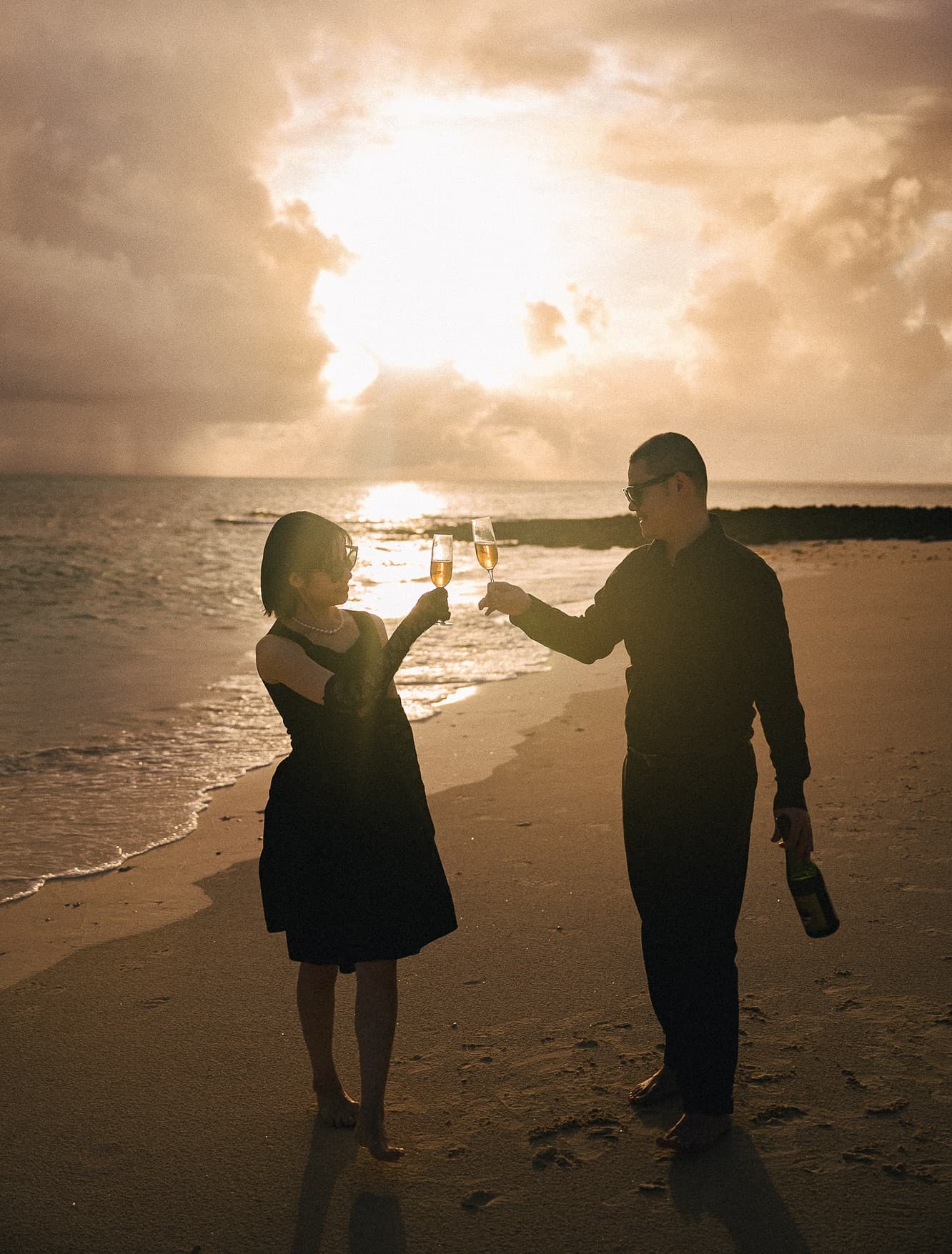 Couple toasting champagne on a Miyakojima beach at golden sunset