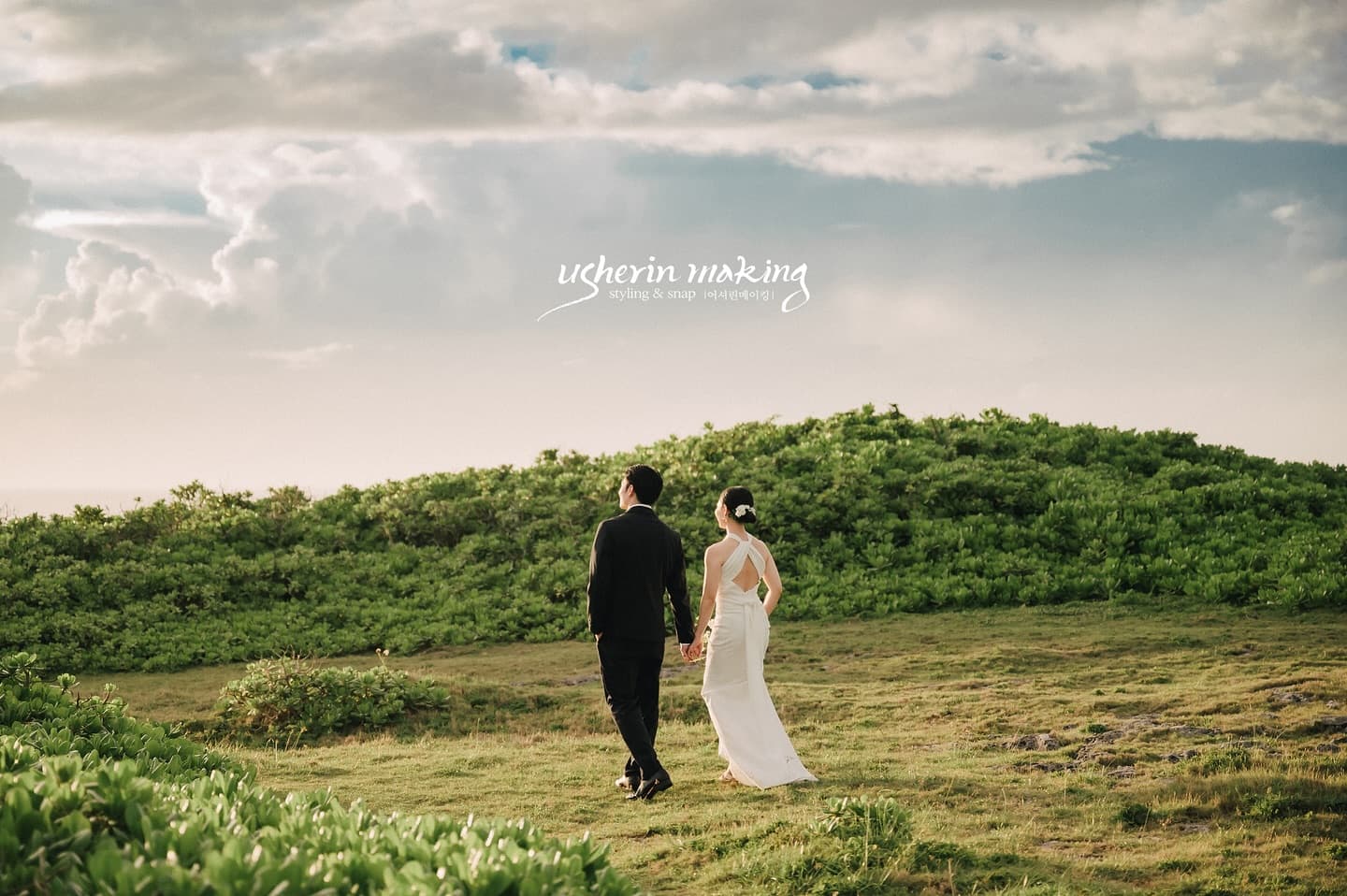 Back view of a couple in black suit and white dress walking up a sunlit hill in Okinawa