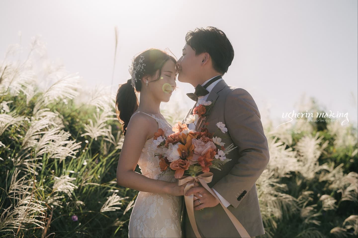 Groom kissing his bride's forehead amid sunlit pampas grass, Okinawa