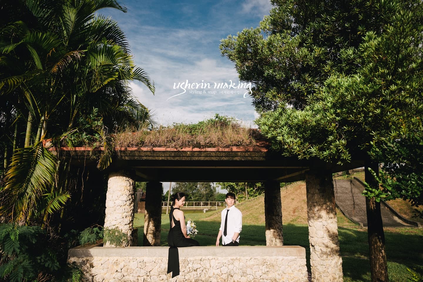 Couple facing each other in a grass-roofed stone pavilion under blue sky on Miyako Island, Okinawa