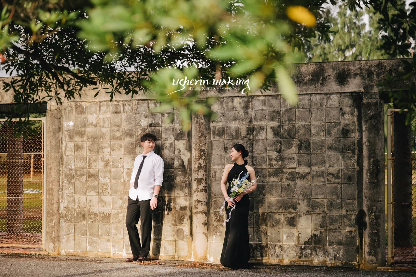 Couple leaning on an old block wall under leafy branches on Miyako Island, Okinawa