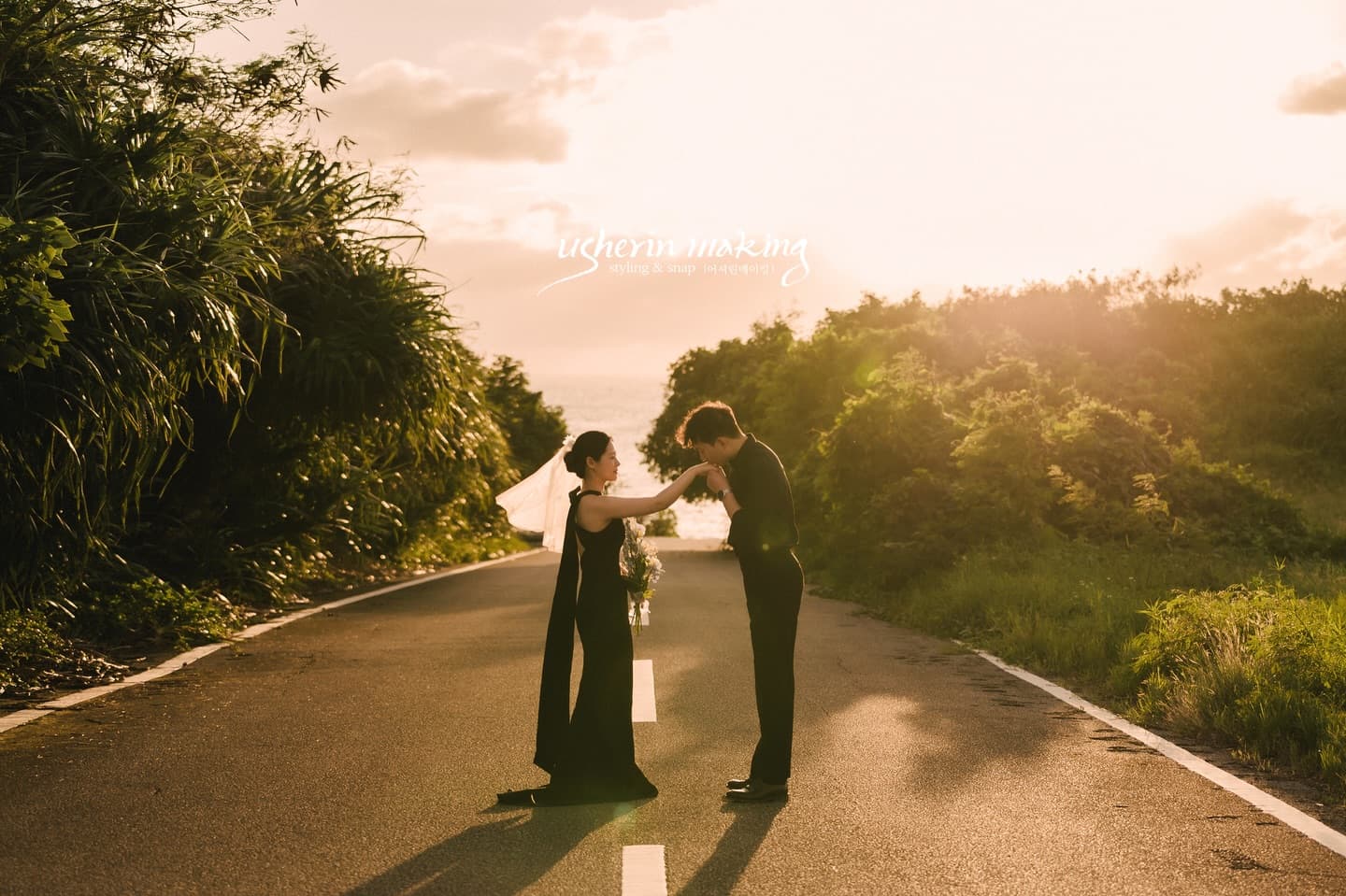 Groom kissing the bride's hand on a sunlit country road at golden hour in Miyakojima