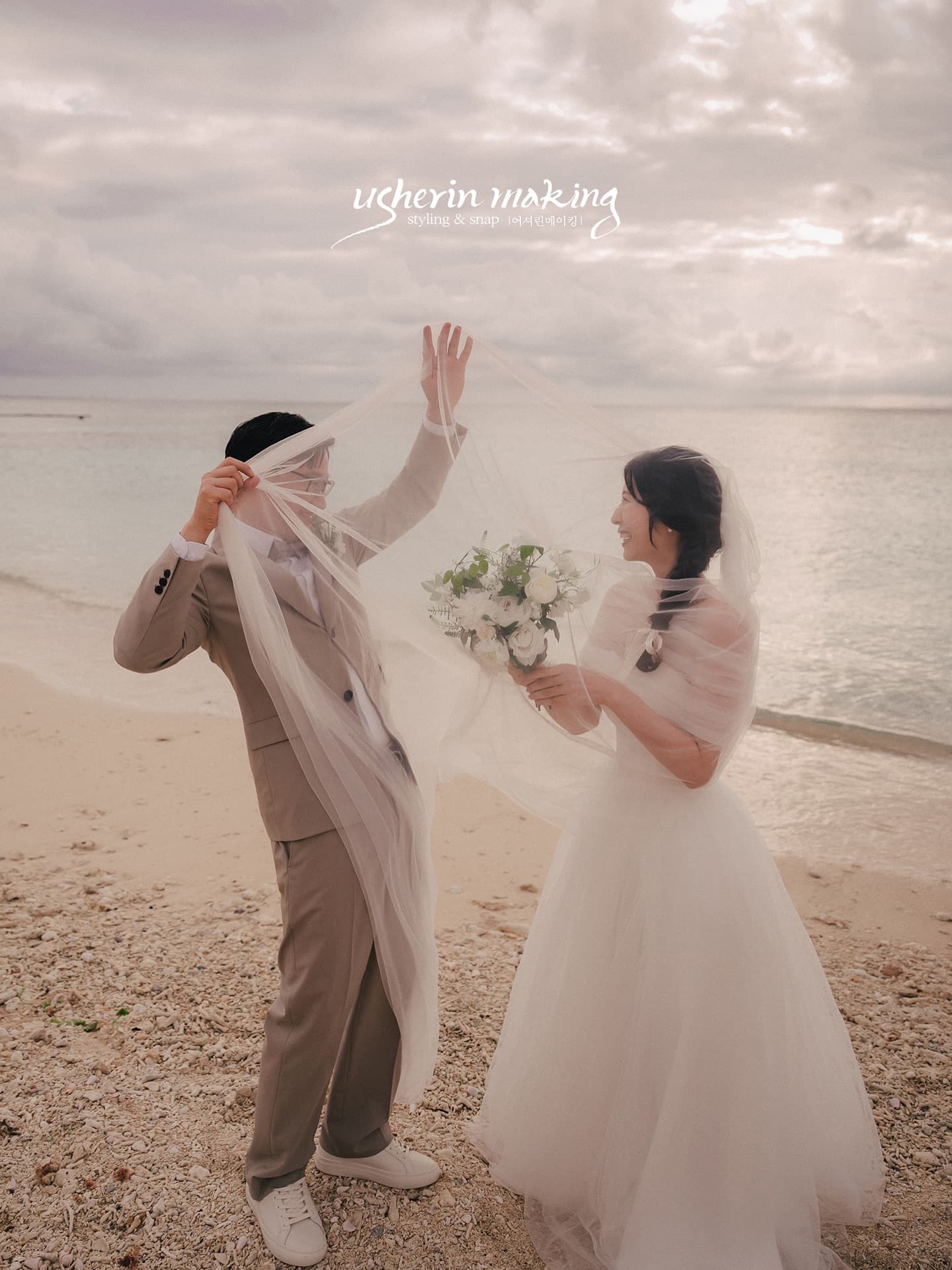 Groom playfully draped in the veil as the bride laughs on an Okinawa beach