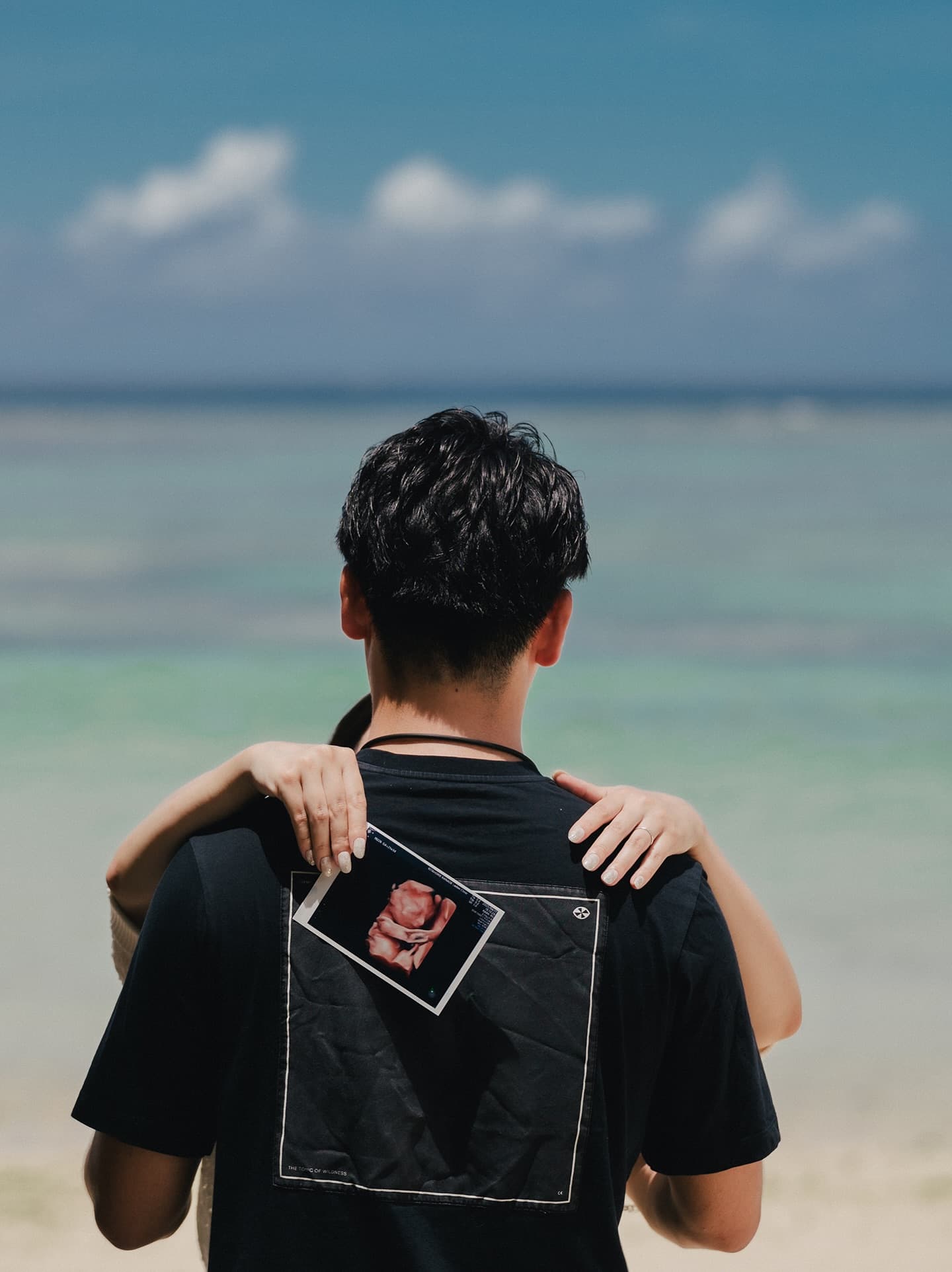 Couple embracing with an ultrasound photo by the blue Okinawa sea