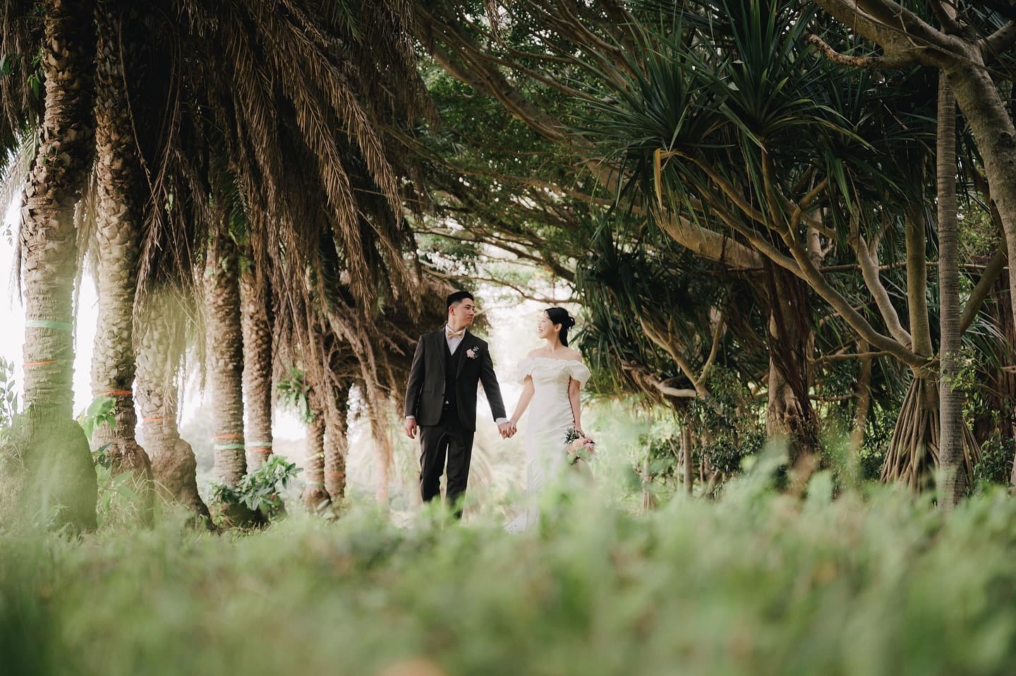 Bride and groom walk hand in hand through an Okinawa palm grove
