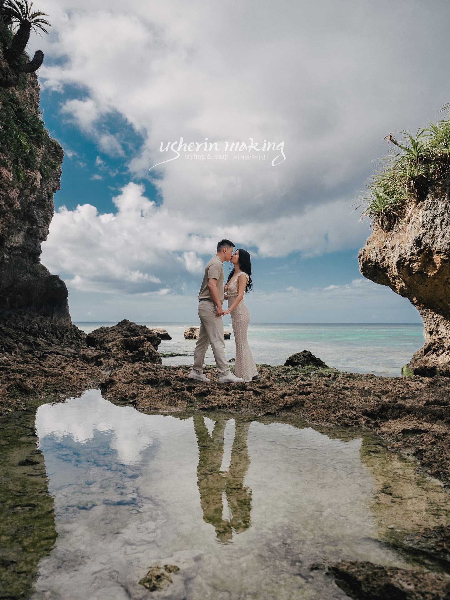 A couple kisses on tidal rocks, mirrored in a pool, on the Okinawa coast