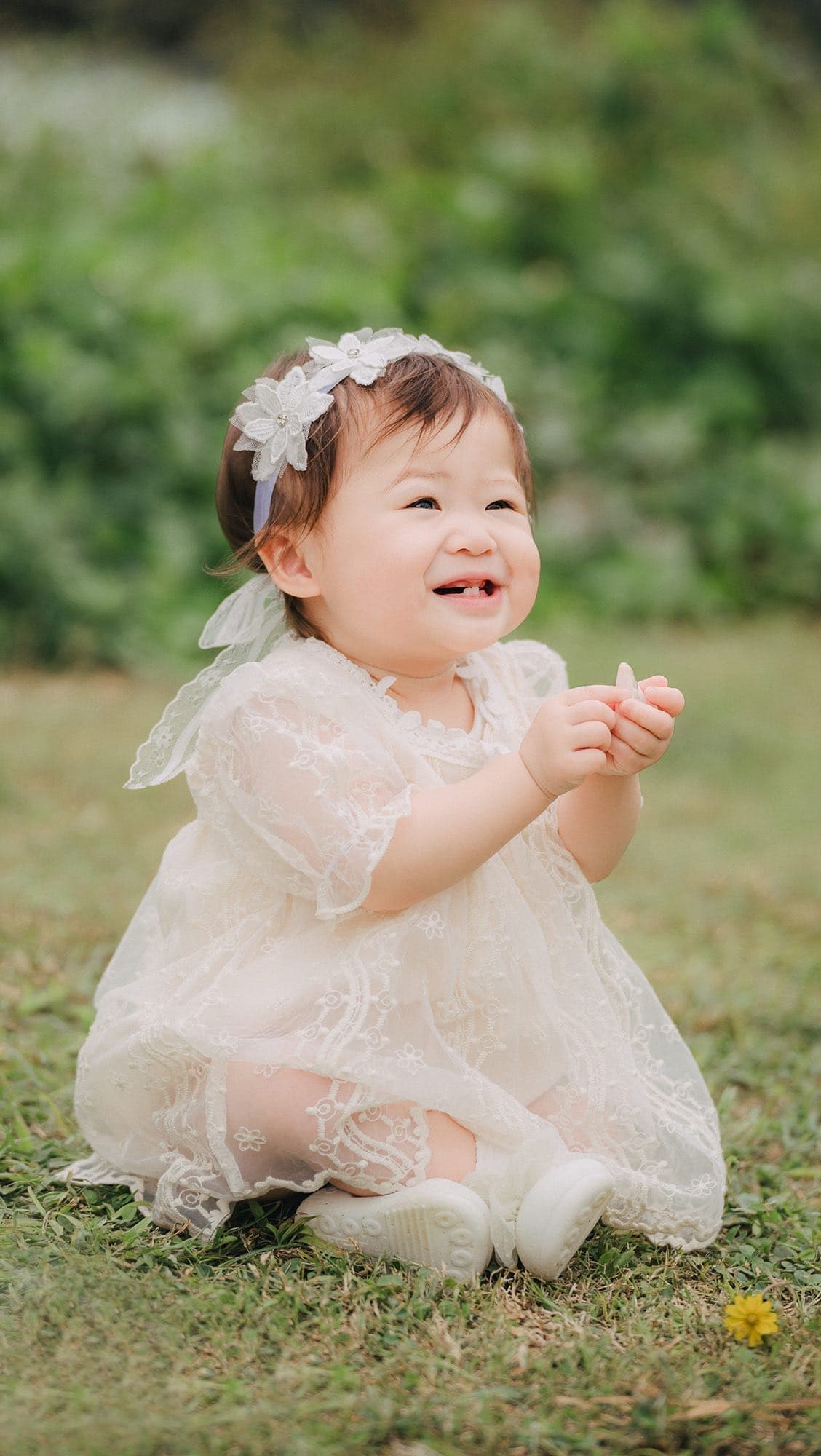 Smiling baby girl in a lace dress sitting on the grass in Okinawa