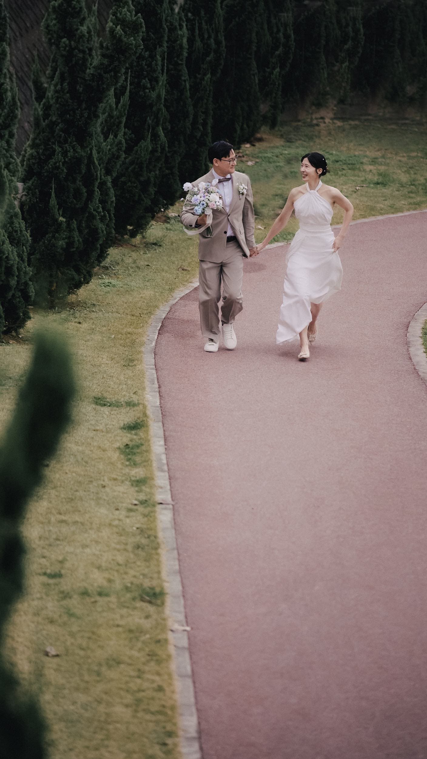 Smiling couple walking hand in hand down a tree-lined garden path in Okinawa