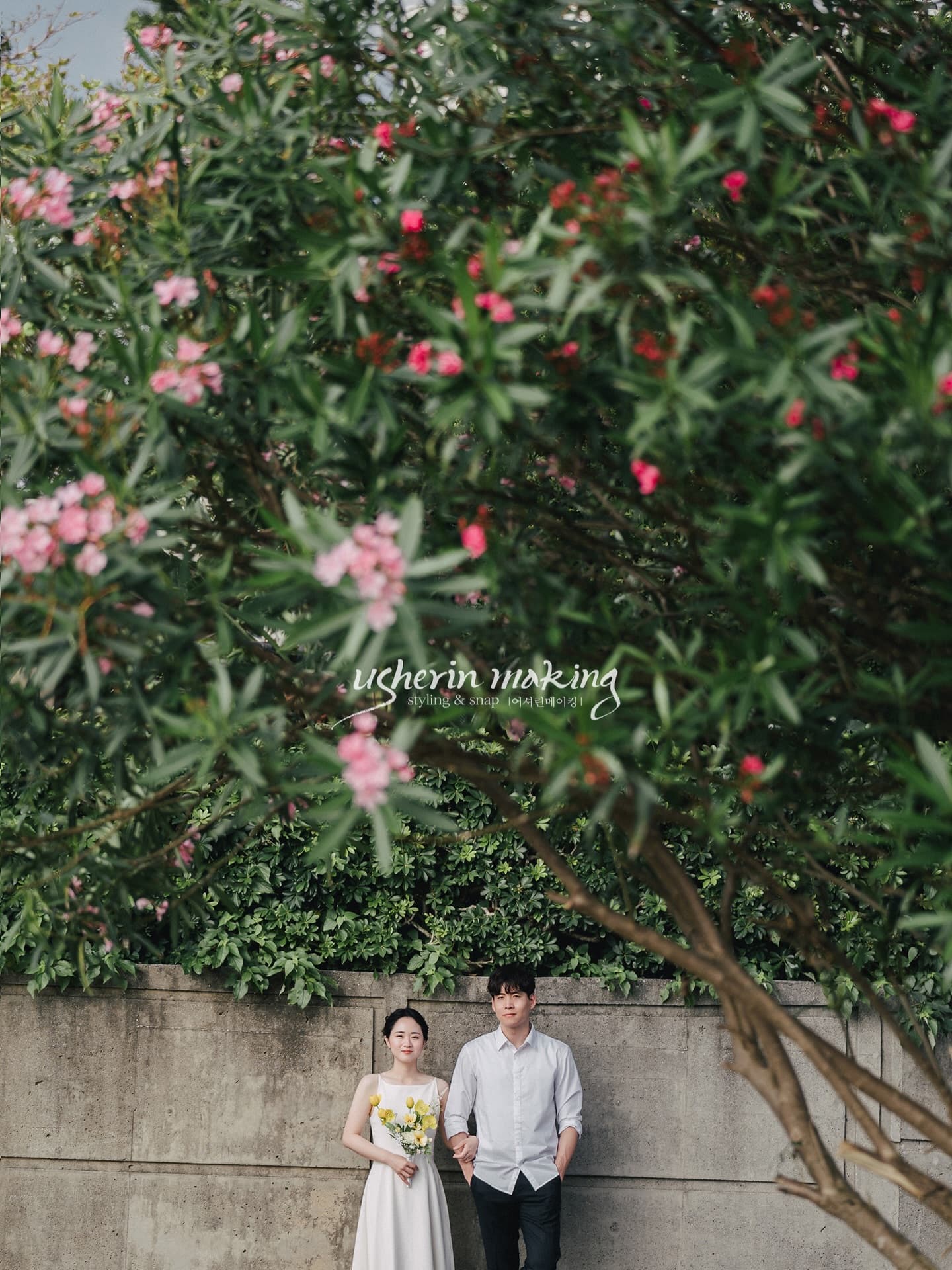 Couple standing beneath a tree of pink blossoms in Okinawa, the bride holding a yellow bouquet