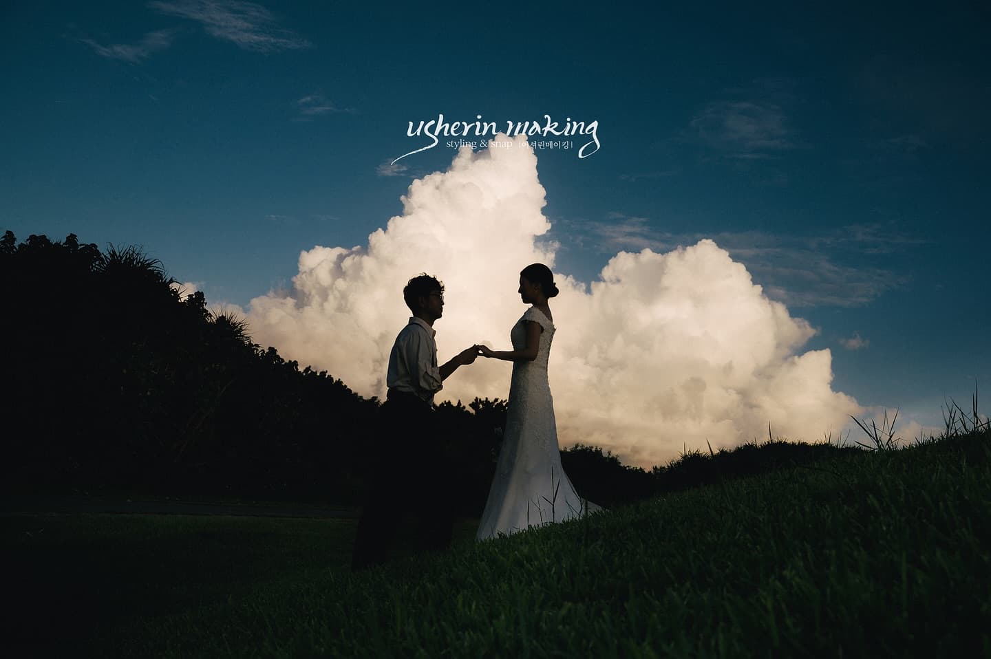 Couple holding hands on a grassy hill under towering clouds in Okinawa