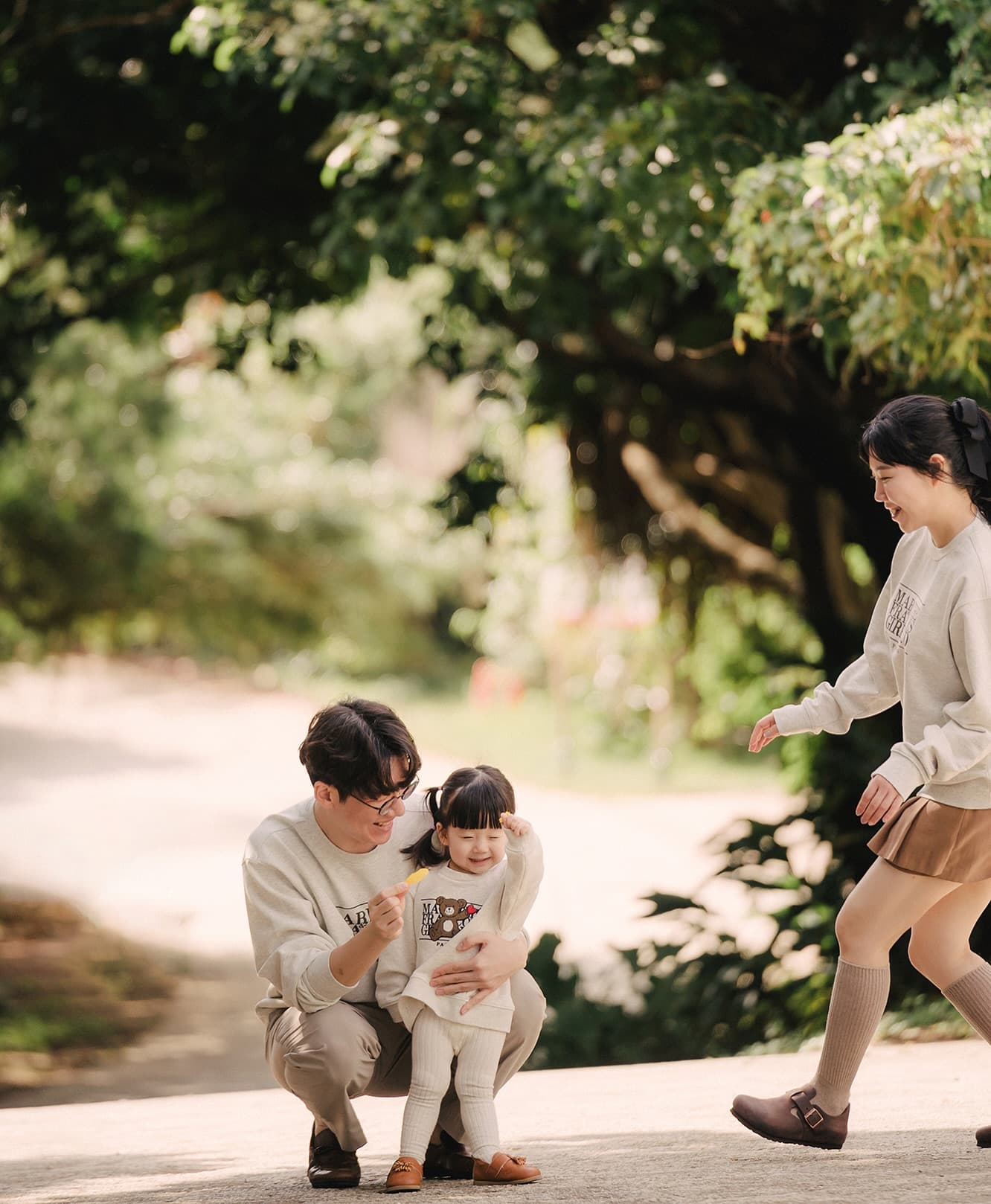 Dad crouching with his little girl on a sunlit tree-lined path in Okinawa