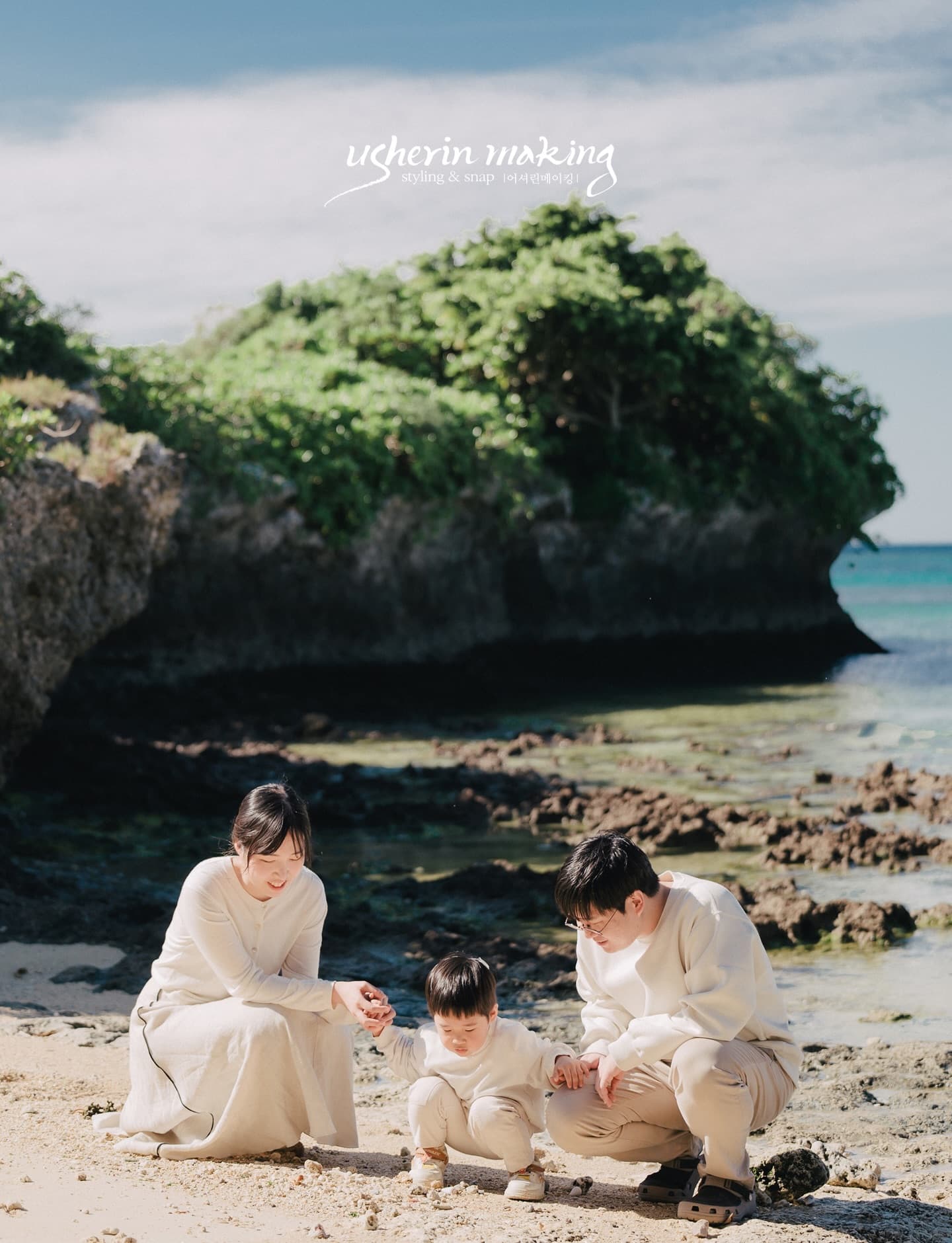 Family of three exploring tide pools beside a mossy rock formation on an Okinawa beach