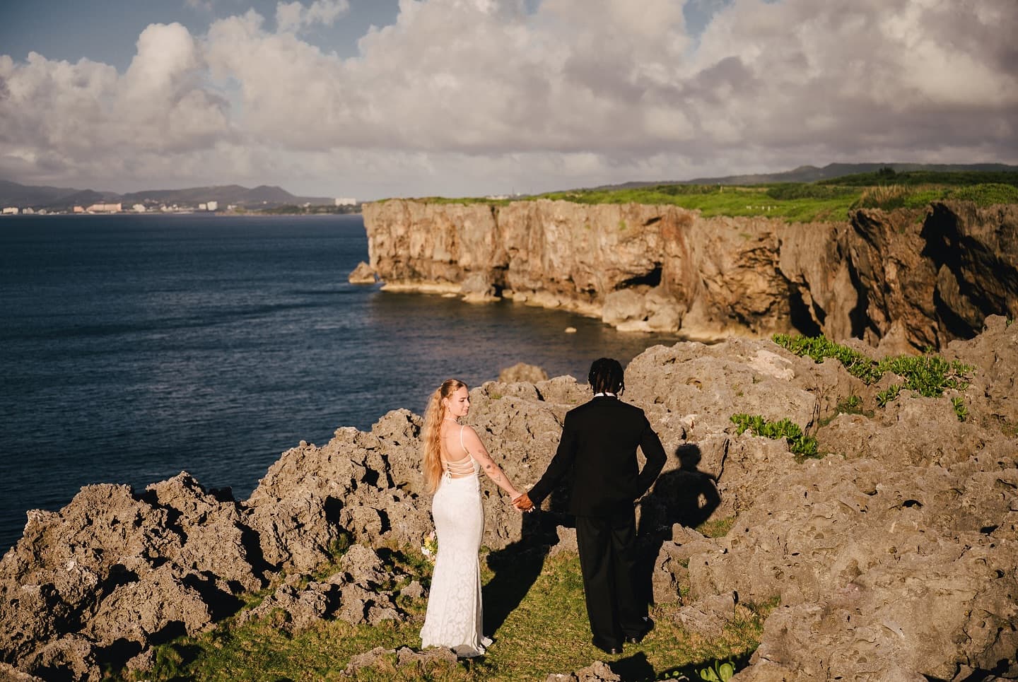 Bride and groom walking hand in hand across rocky cliffs above the deep blue sea in Okinawa