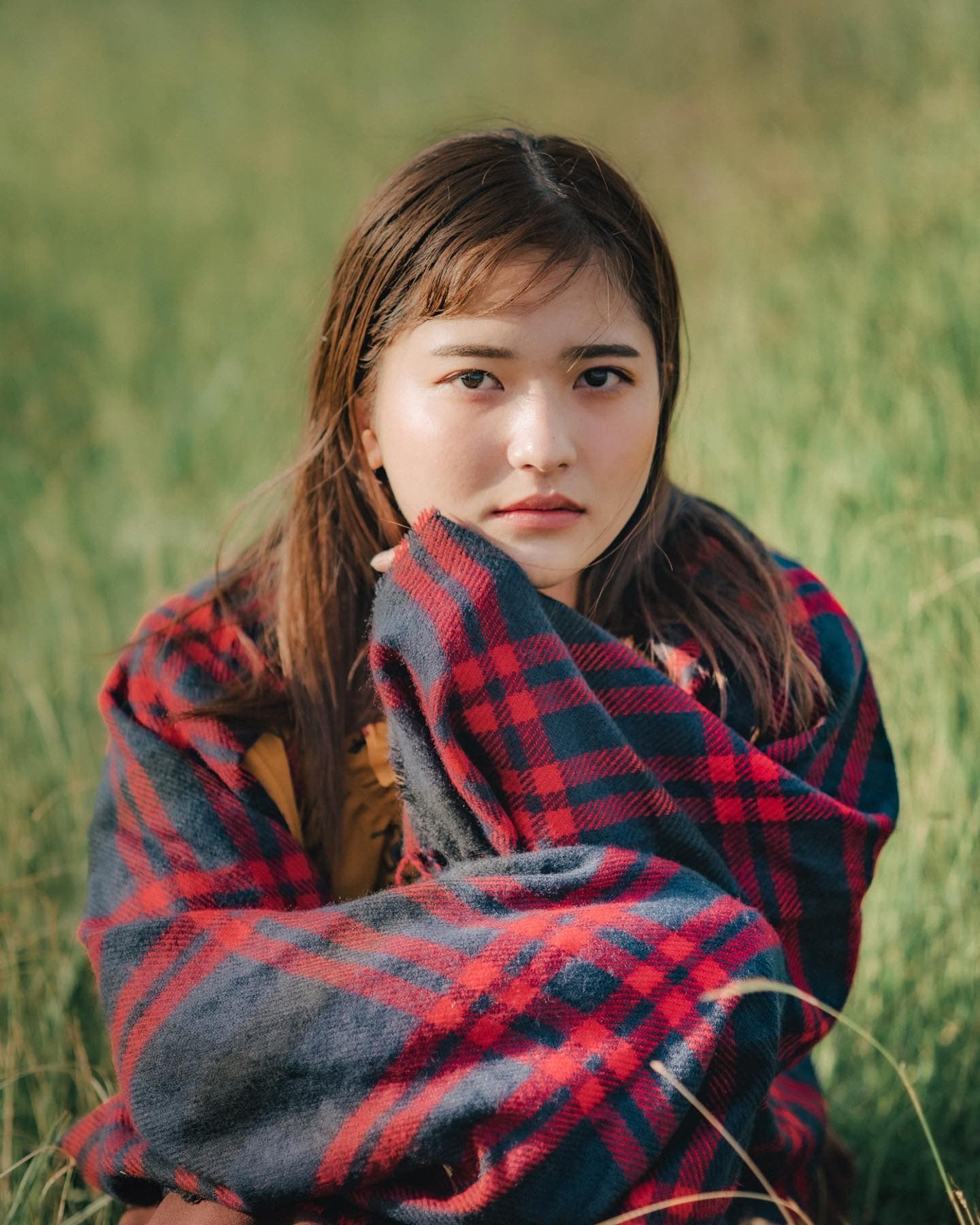 Woman in a plaid blanket looking at the camera in a green field in Okinawa