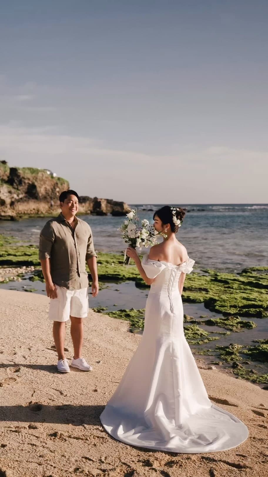 Bride holding a bouquet facing a smiling man on an Okinawa beach