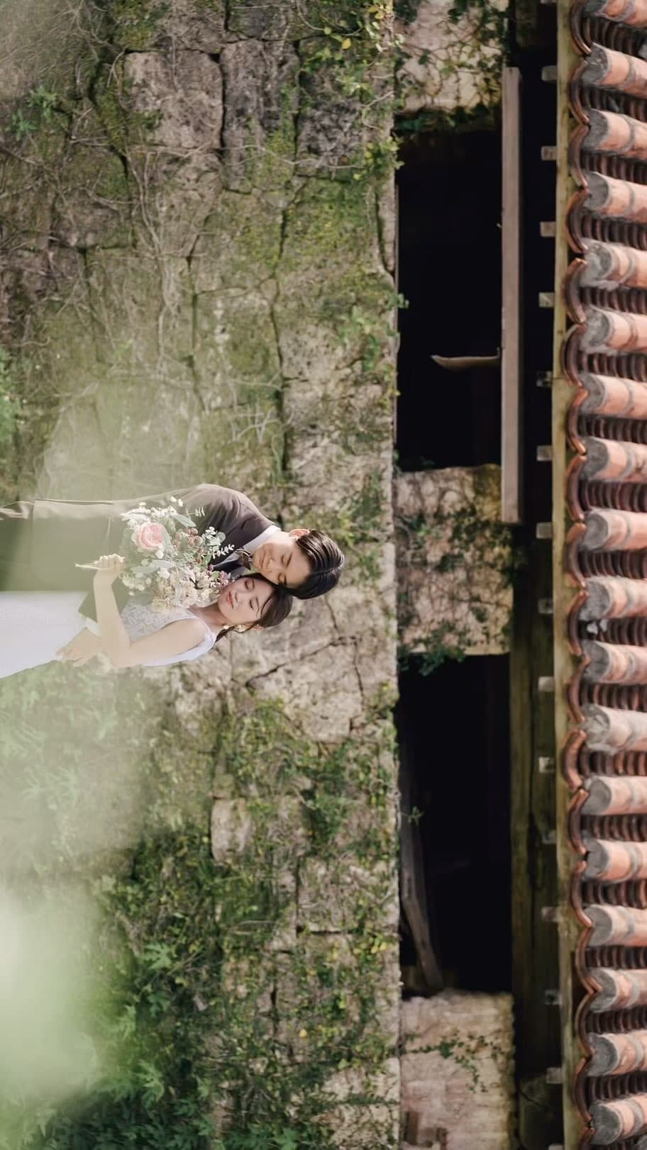 Couple nestled together by a mossy stone wall and red-tiled roof in Okinawa