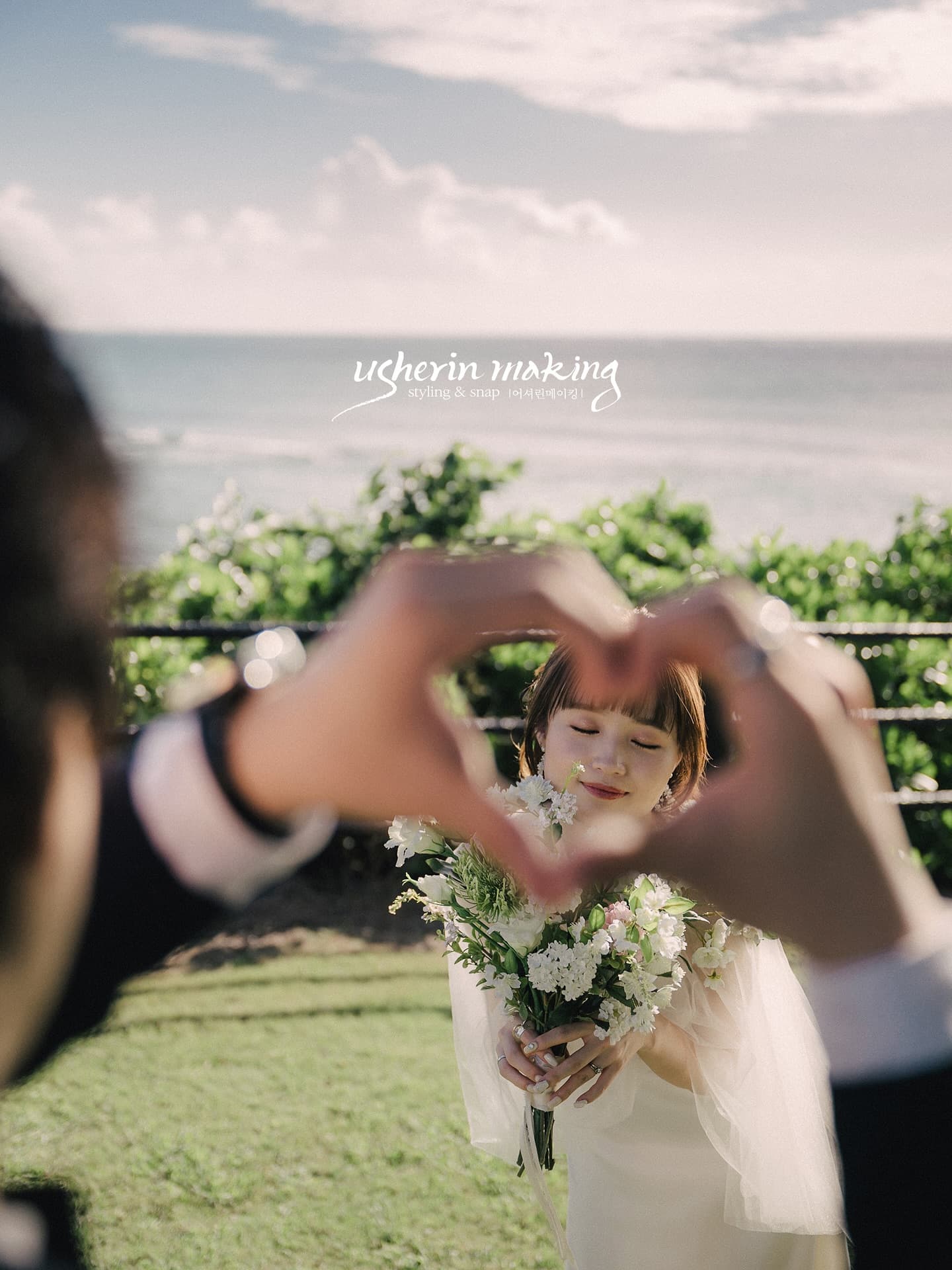Smiling bride framed by heart-shaped hands with the Okinawa sea behind