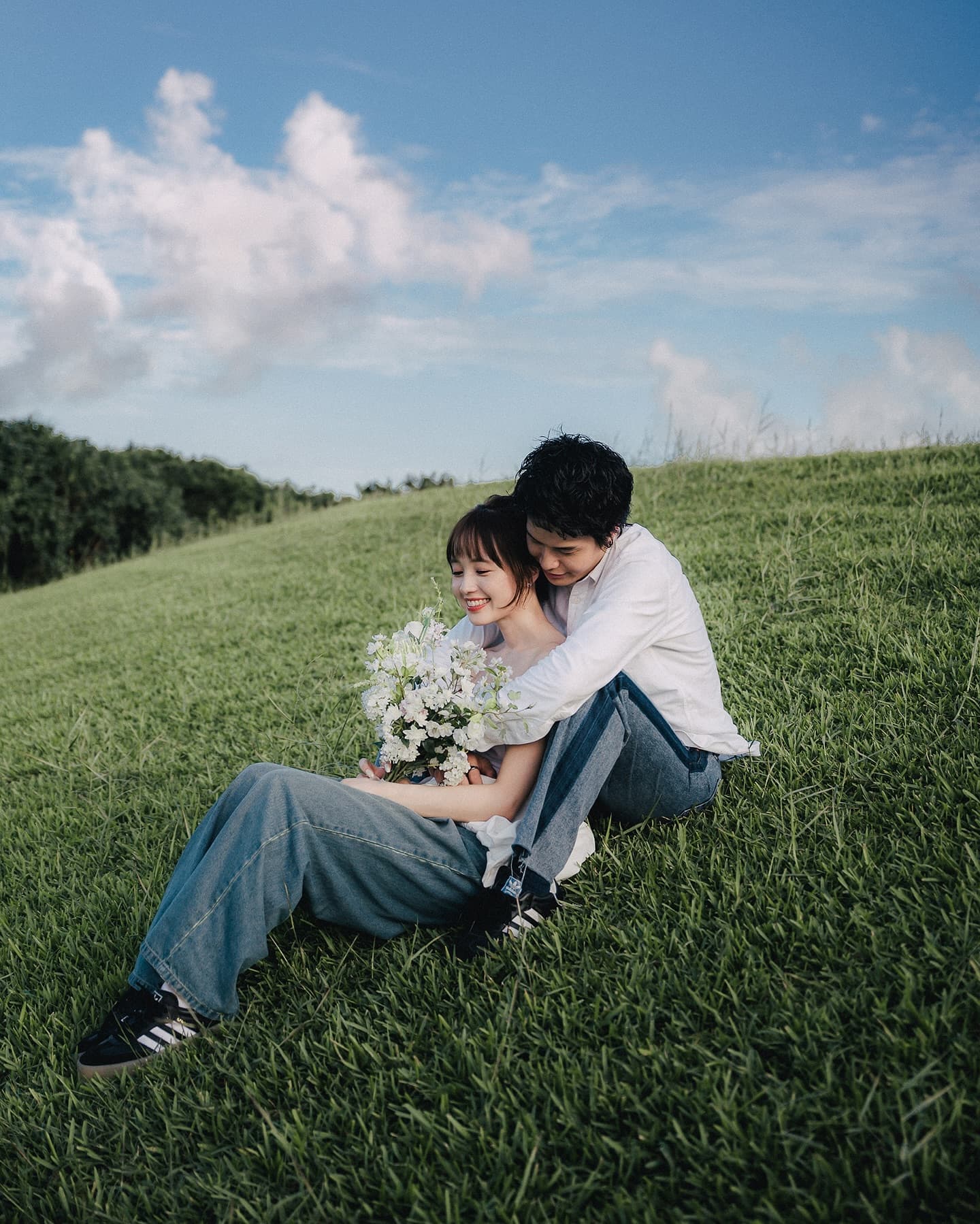Couple sitting close on a grassy Okinawa hill under a blue sky