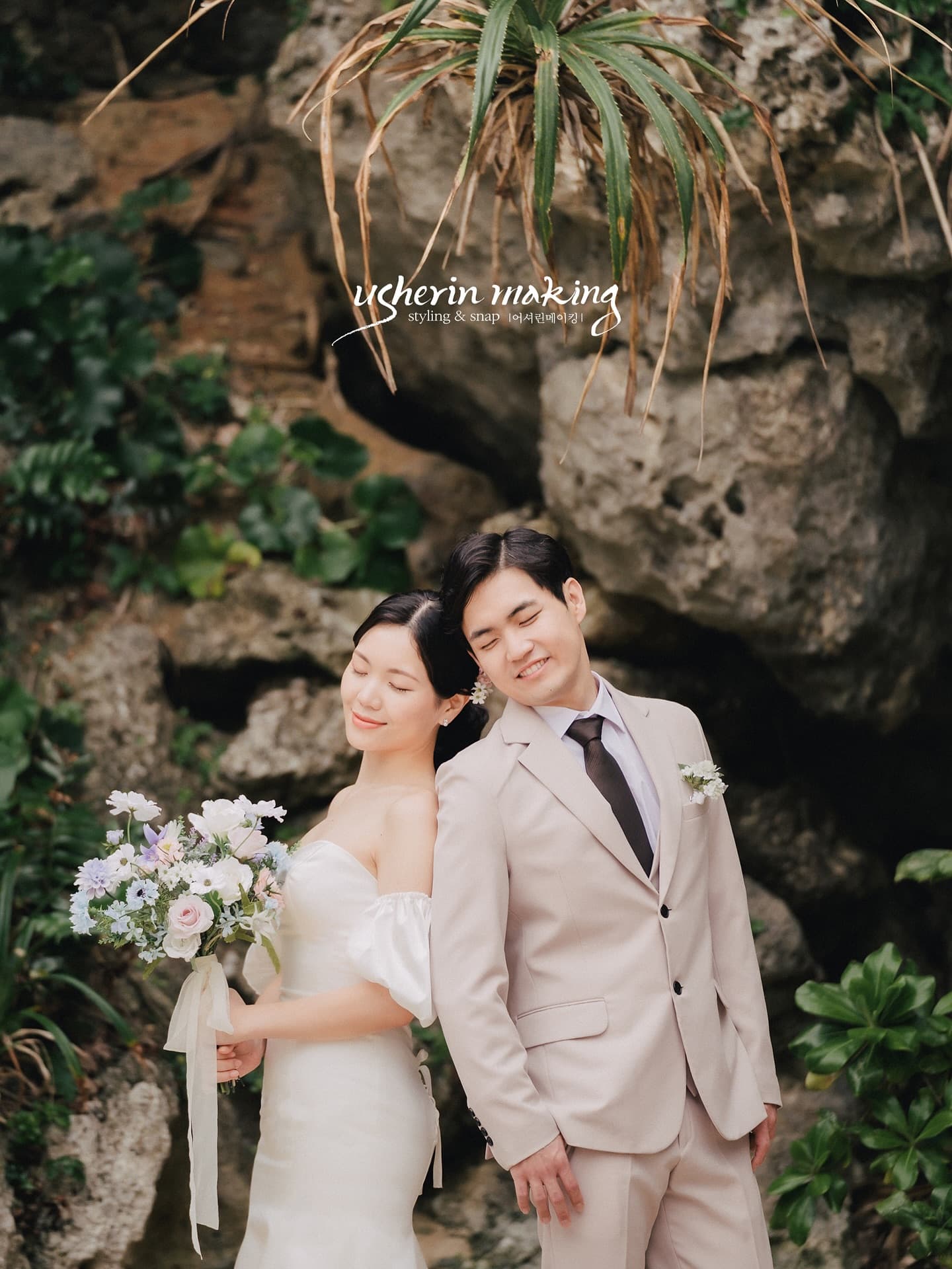 Couple leaning close by a plant-draped rock wall with a pastel bouquet, Okinawa