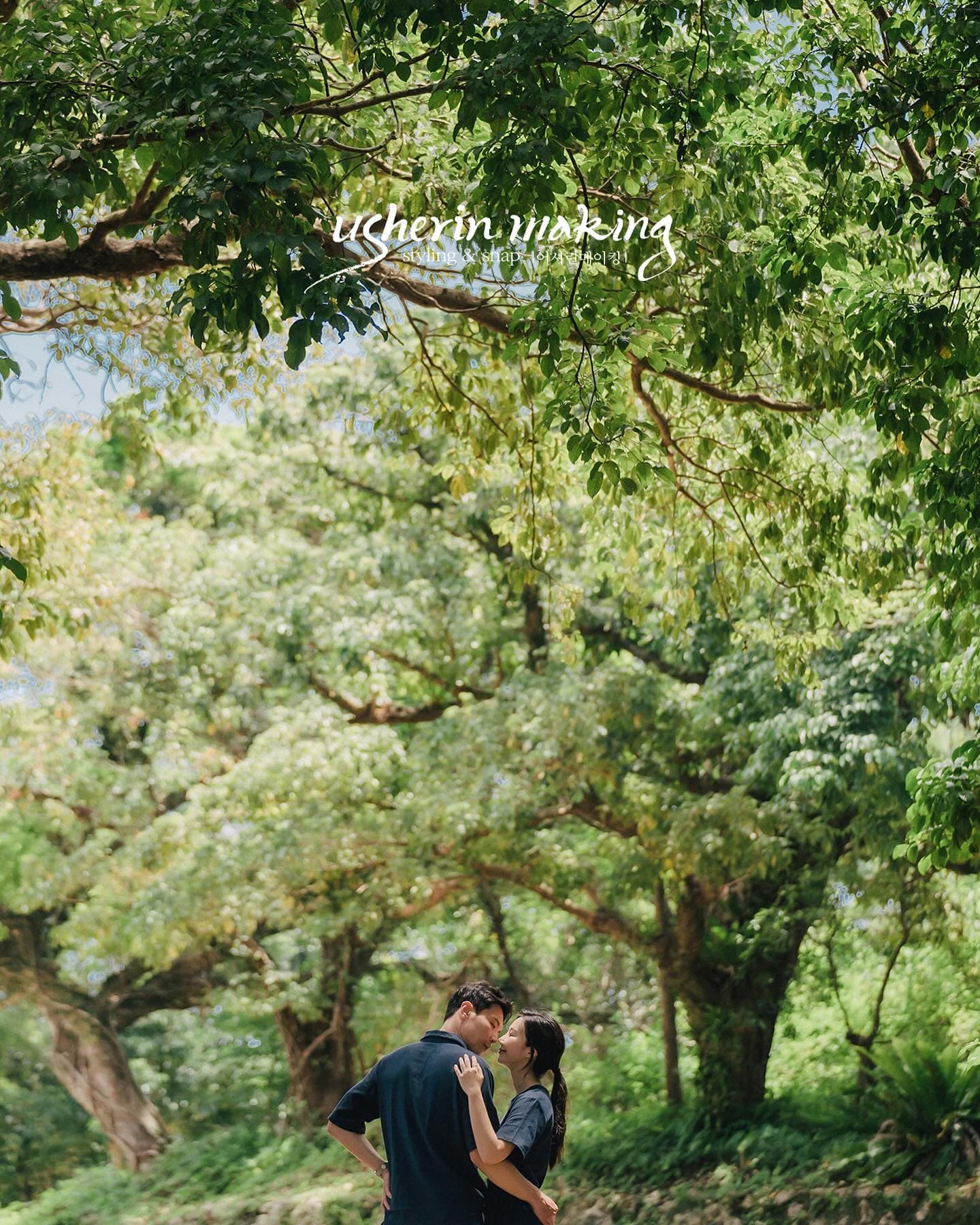 A couple embracing beneath lush green trees on a forest path in Okinawa