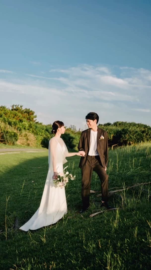 Couple holding hands in a green meadow under Okinawa's clear blue sky
