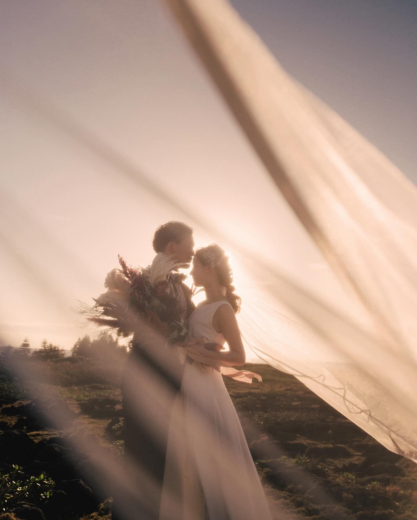 Couple gazing at each other through a flowing veil in golden sunset light in Okinawa
