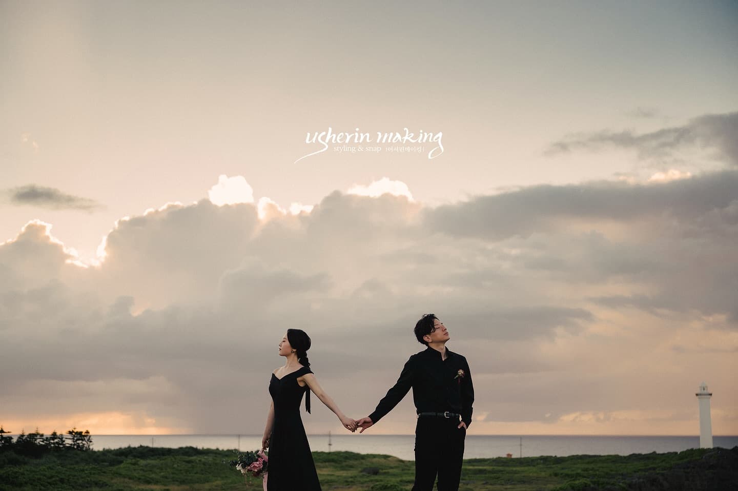 Couple in black holding hands on an Okinawa cape at sunset, lighthouse in the distance