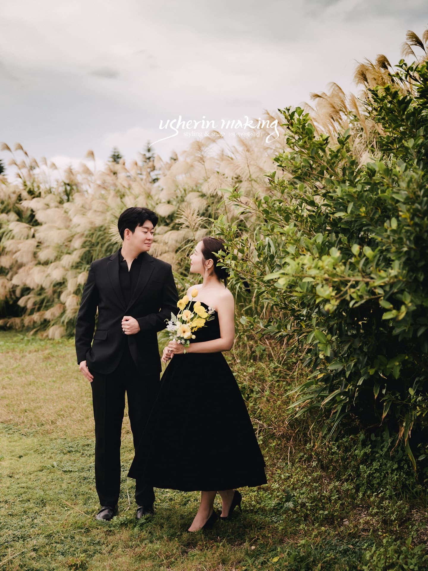 Couple in black holding a yellow bouquet by silver grass in Okinawa