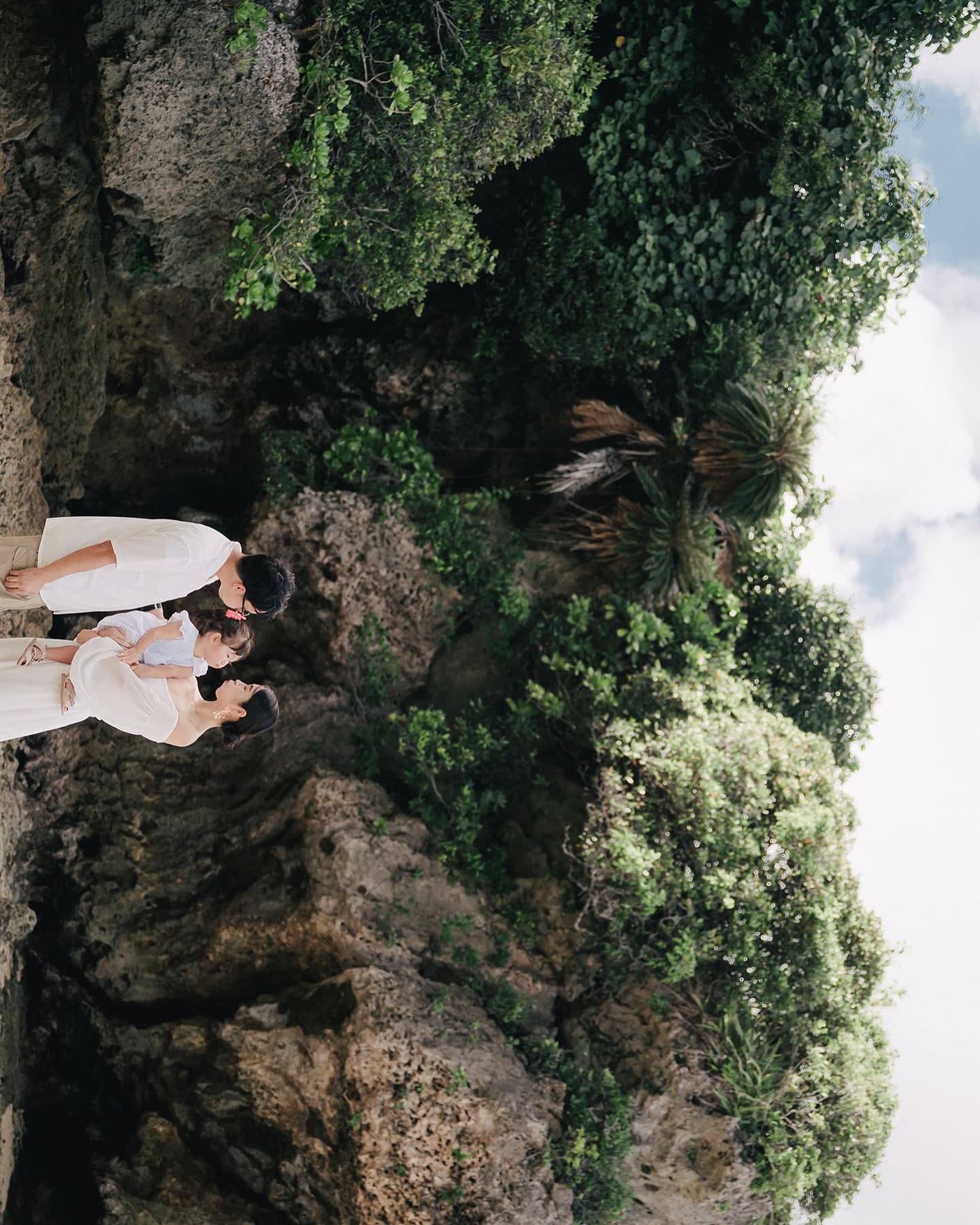 Family holding their girl before rugged rocks and palms in Okinawa