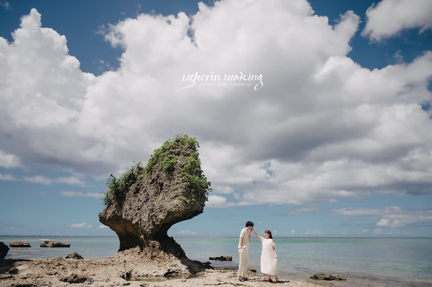 Couple standing by a mushroom-shaped rock on an Okinawa beach under big clouds